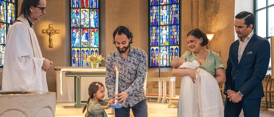 Ett dop i en kyrka. En liten flicka bär ett dopljus för att överlämna till det nydöpta barnet.