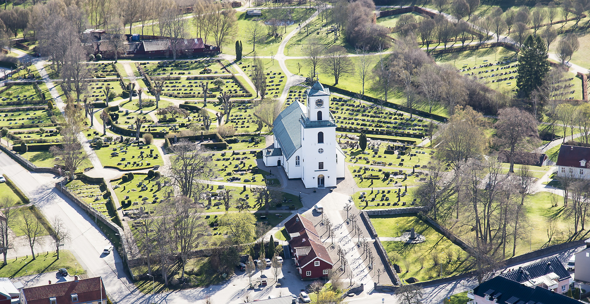 Vit kyrka med torn och koppartak med omgivande kyrkogård och hus.