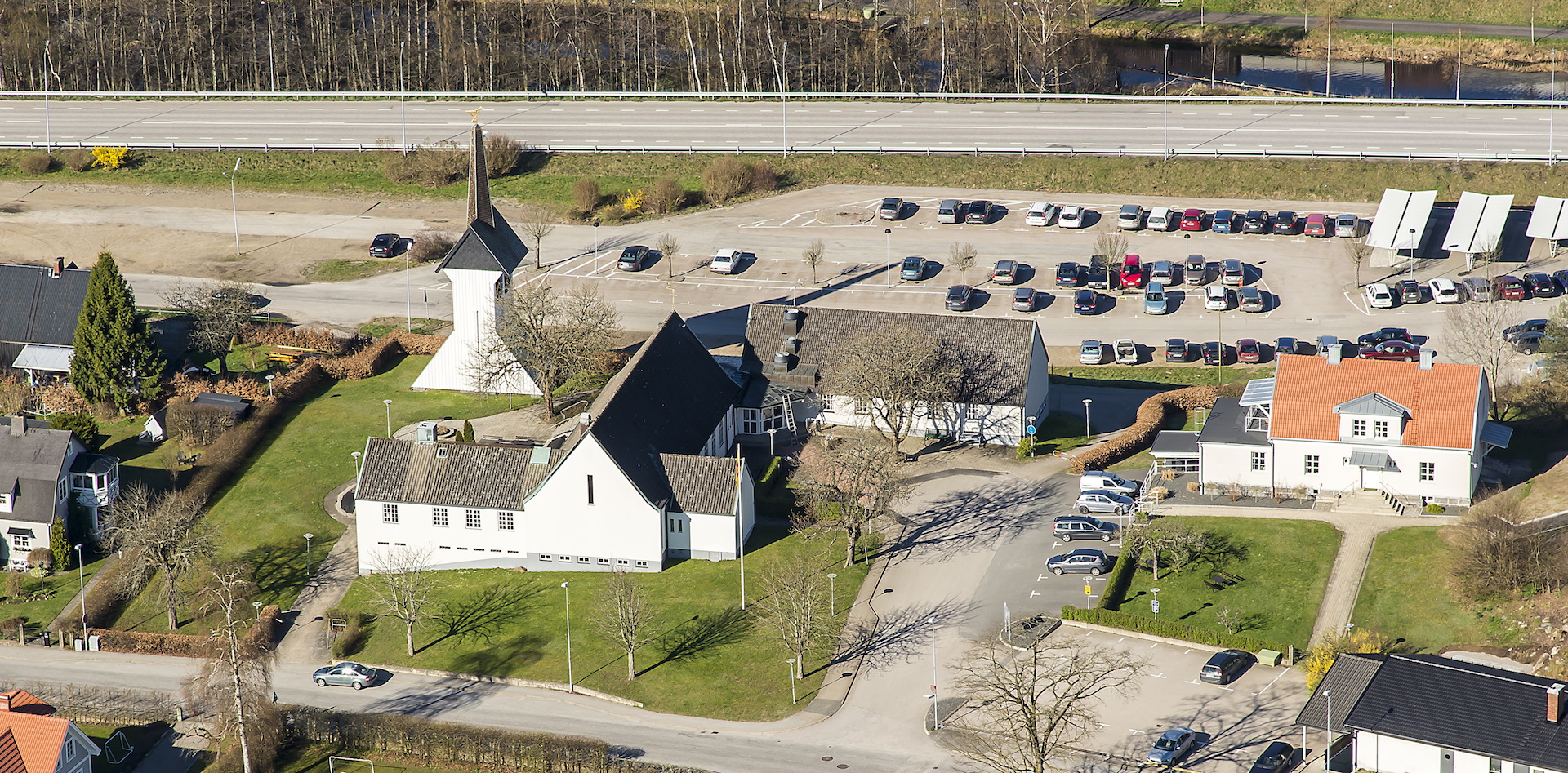 Tre sammanlänkade vita byggnader med svart tak med fristående klockstapel.