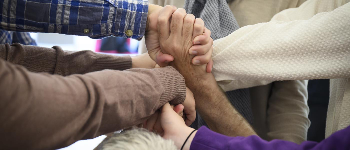 En grupp människor korsar varandras armar och håller händer.