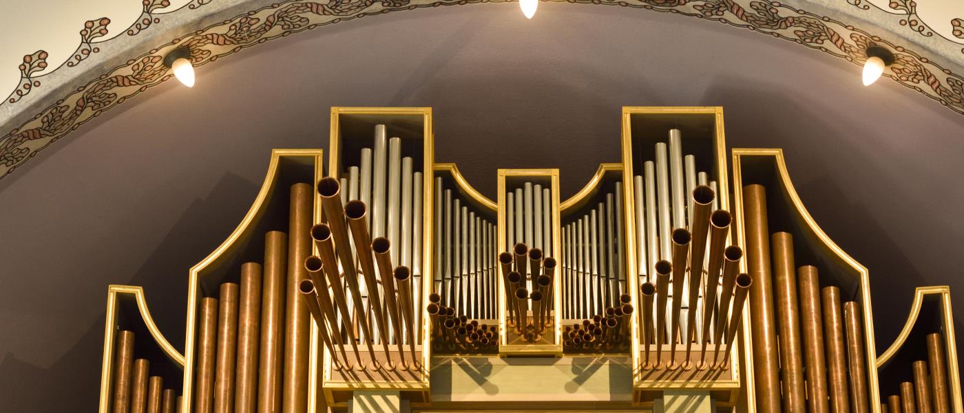 Orgelpipor sticker upp bakom räcket på en orgelläktare.