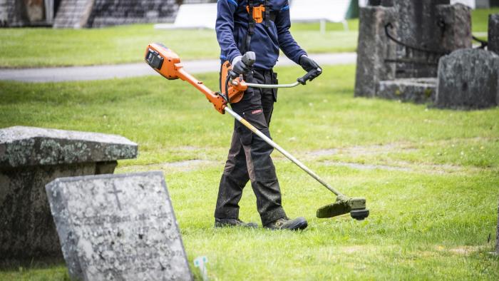 En person går med en grästrimmer mellan gravarna på en kyrkogård.