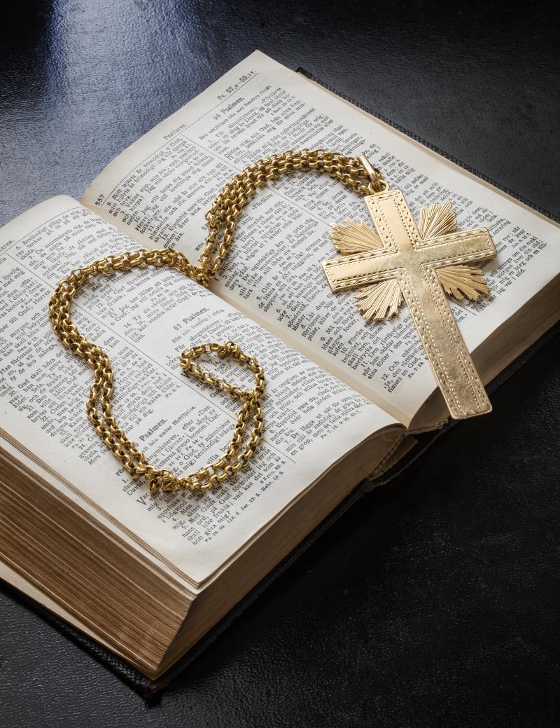 Ett halsband med ett kors av guld ligger i en uppslagen bibel.