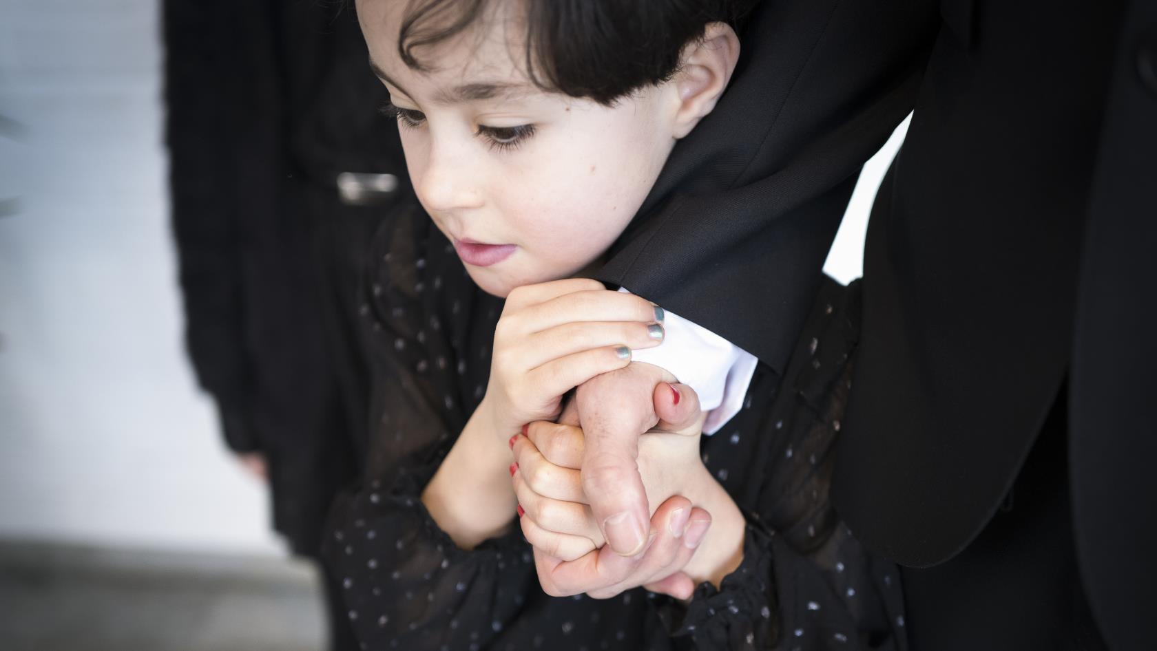 Ett barn håller en vuxens hand med båda händerna.