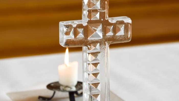 Närbild på ett litet glaskors och ett tänt ljus på ett altare.