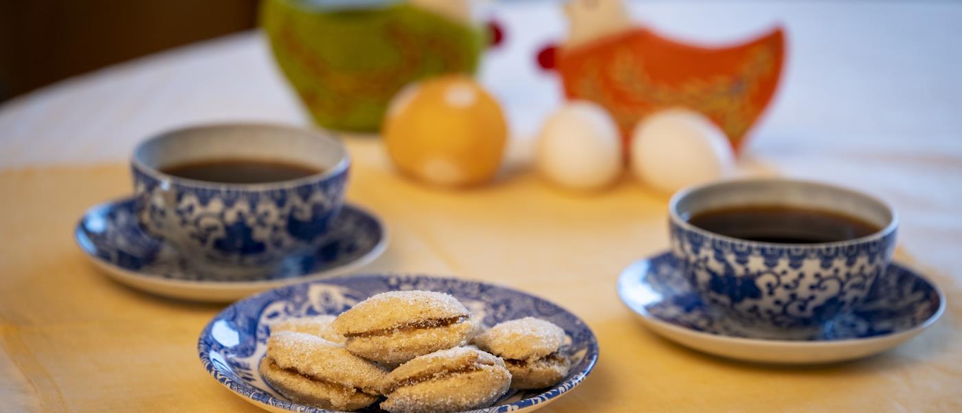 Ett kakfat, två kaffekoppar på fat och två påskhönor med ägg står uppdukade på en gul duk.