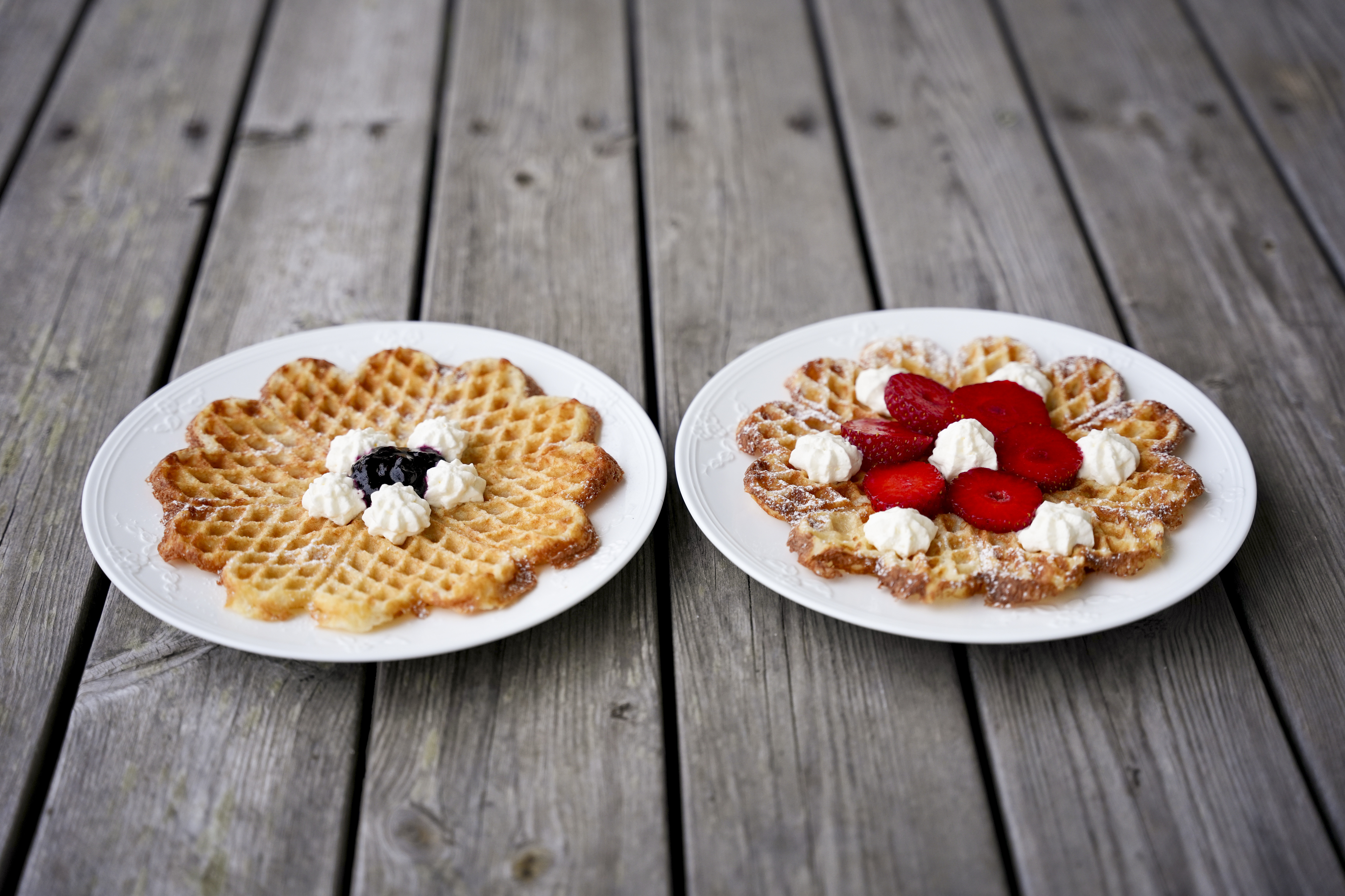 Två tallrikar med våfflor med sylt och grädde står på ett bord av obehandlat trä.