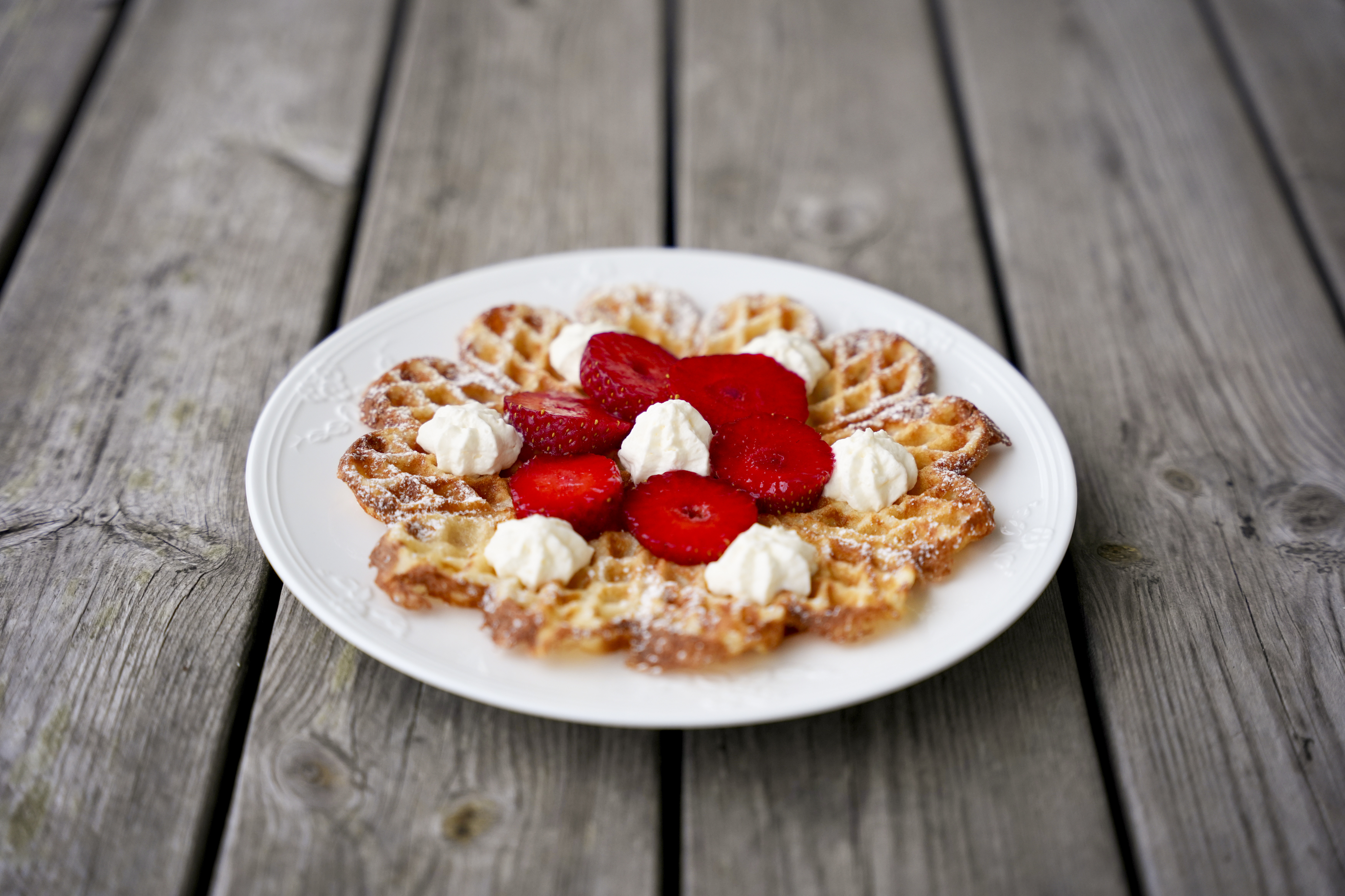 En tallrik med våfflor med jordgubbar och grädde står på ett bord av obehandlat trä.