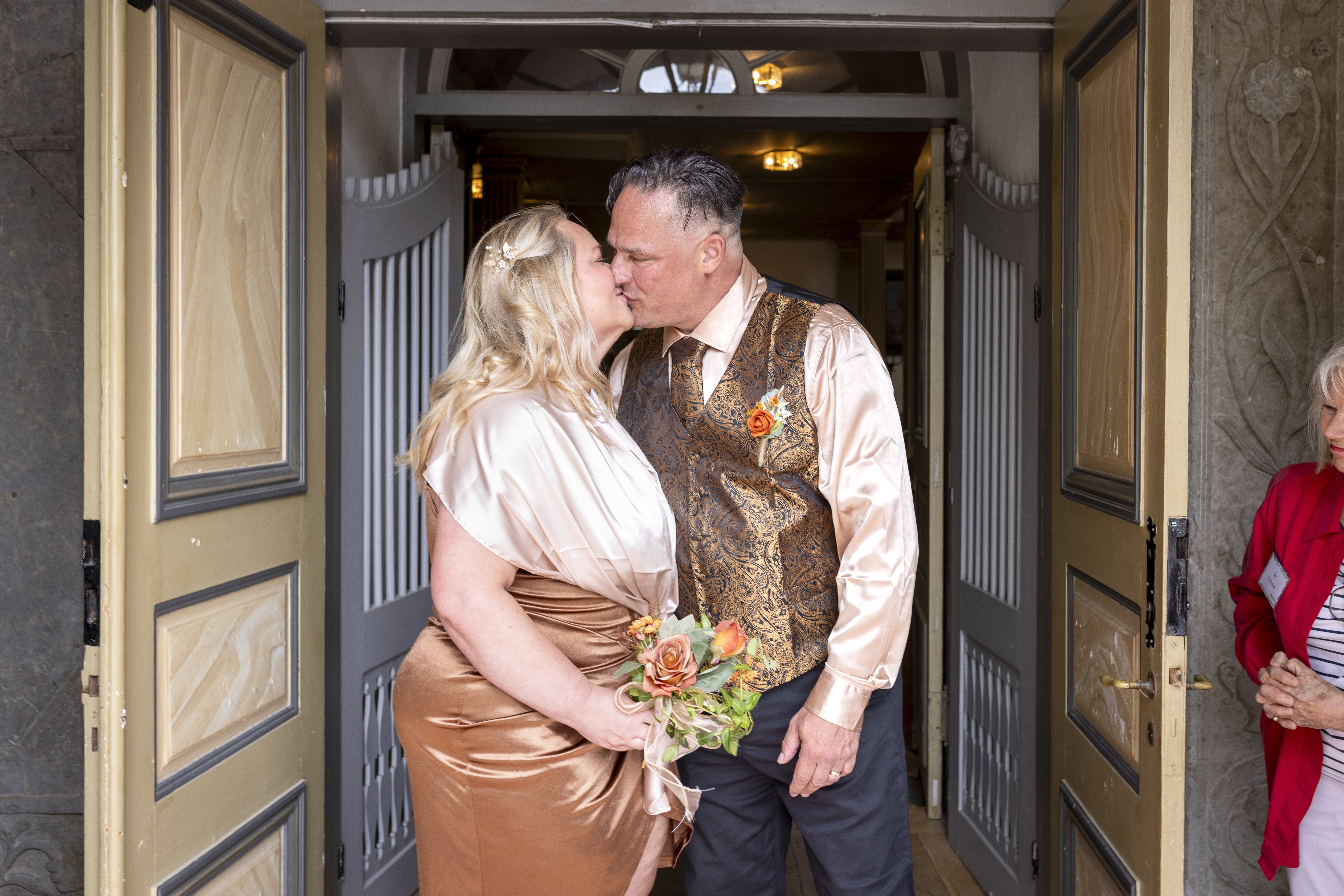 Drop-in vigsel i en kyrka. Ett brudpar står i en dörröppning och kysser varandra. Bruden håller en blombukett i handen.