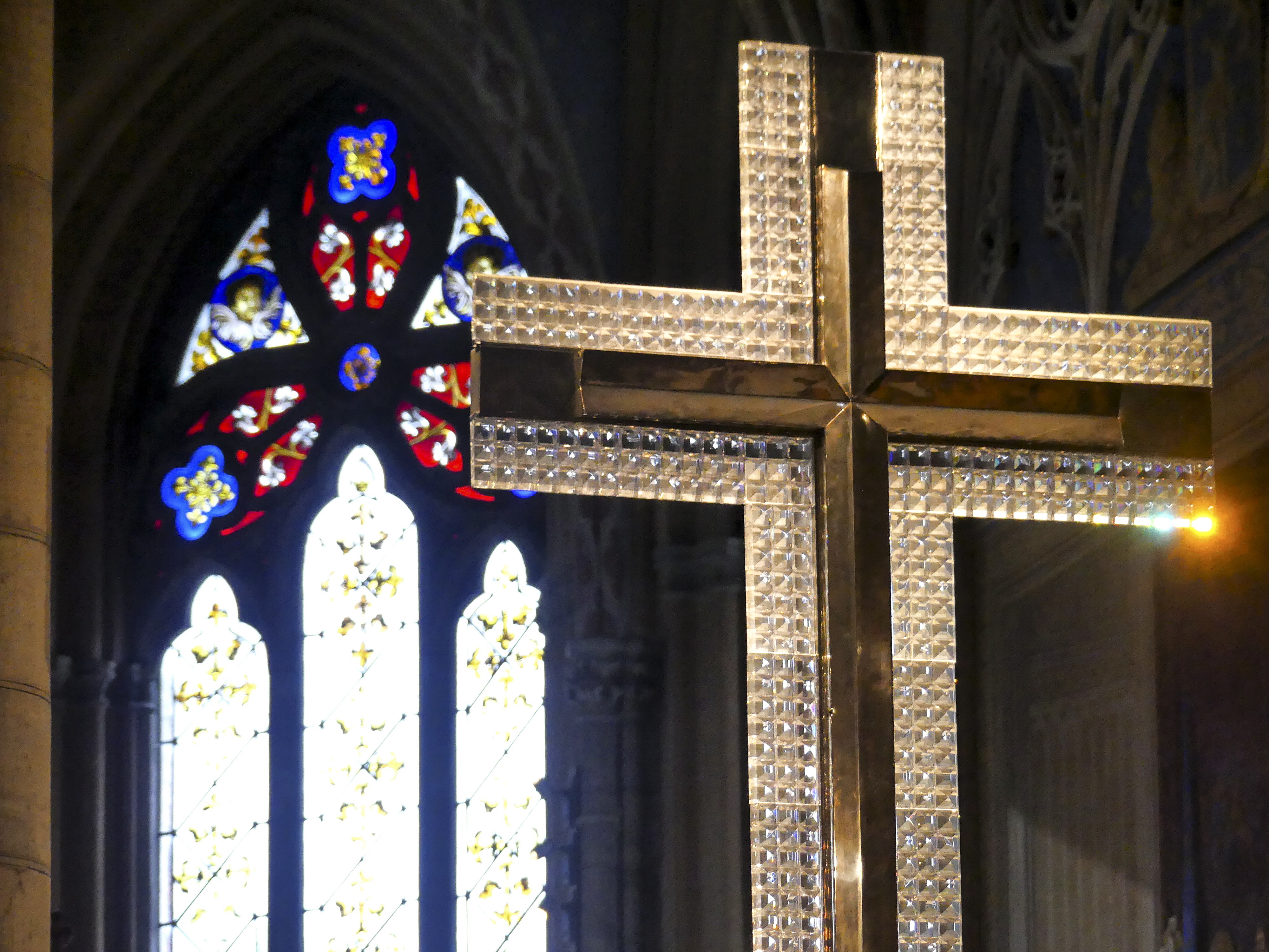 Närbild på altarkorset av kristall i Uppsala domkyrka. Ett stort upplyst kyrkfönster i bakgrunden.