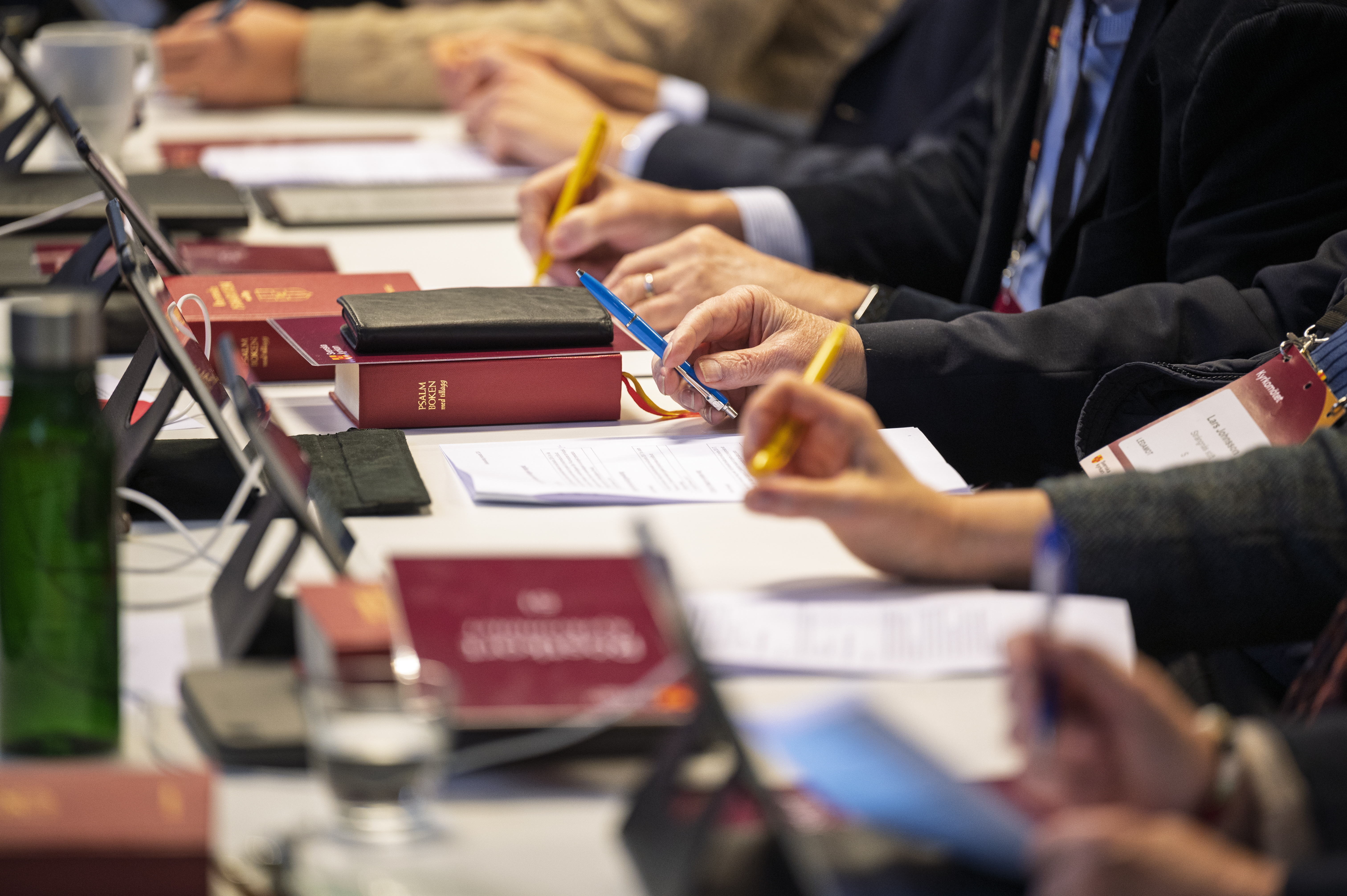 Flera personer sitter vid ett bord med en penna i handen. Biblar och papper ligger på bordet.