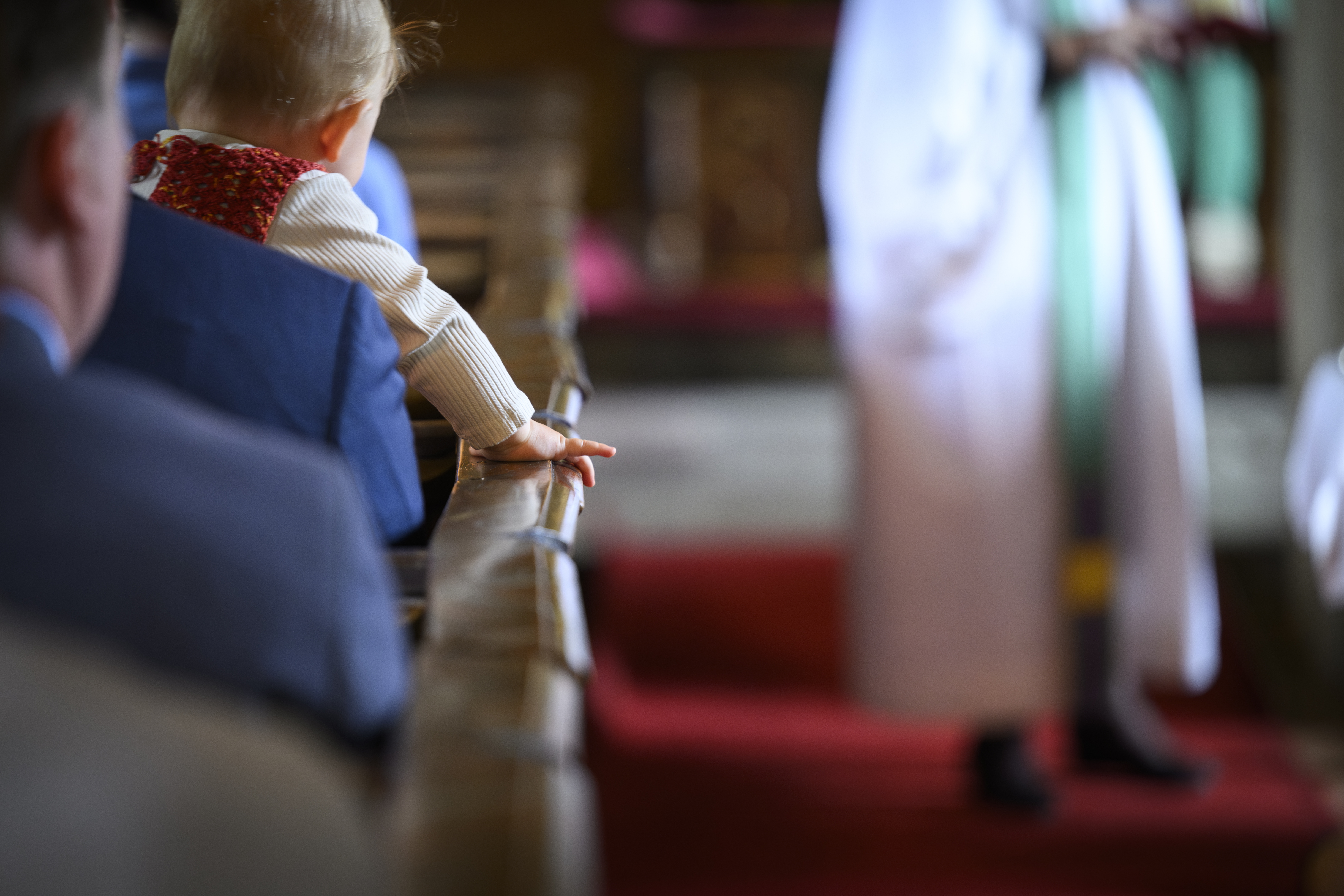 Ett litet barn sitter i knät på en person och håller i kyrkbänksdörren.
