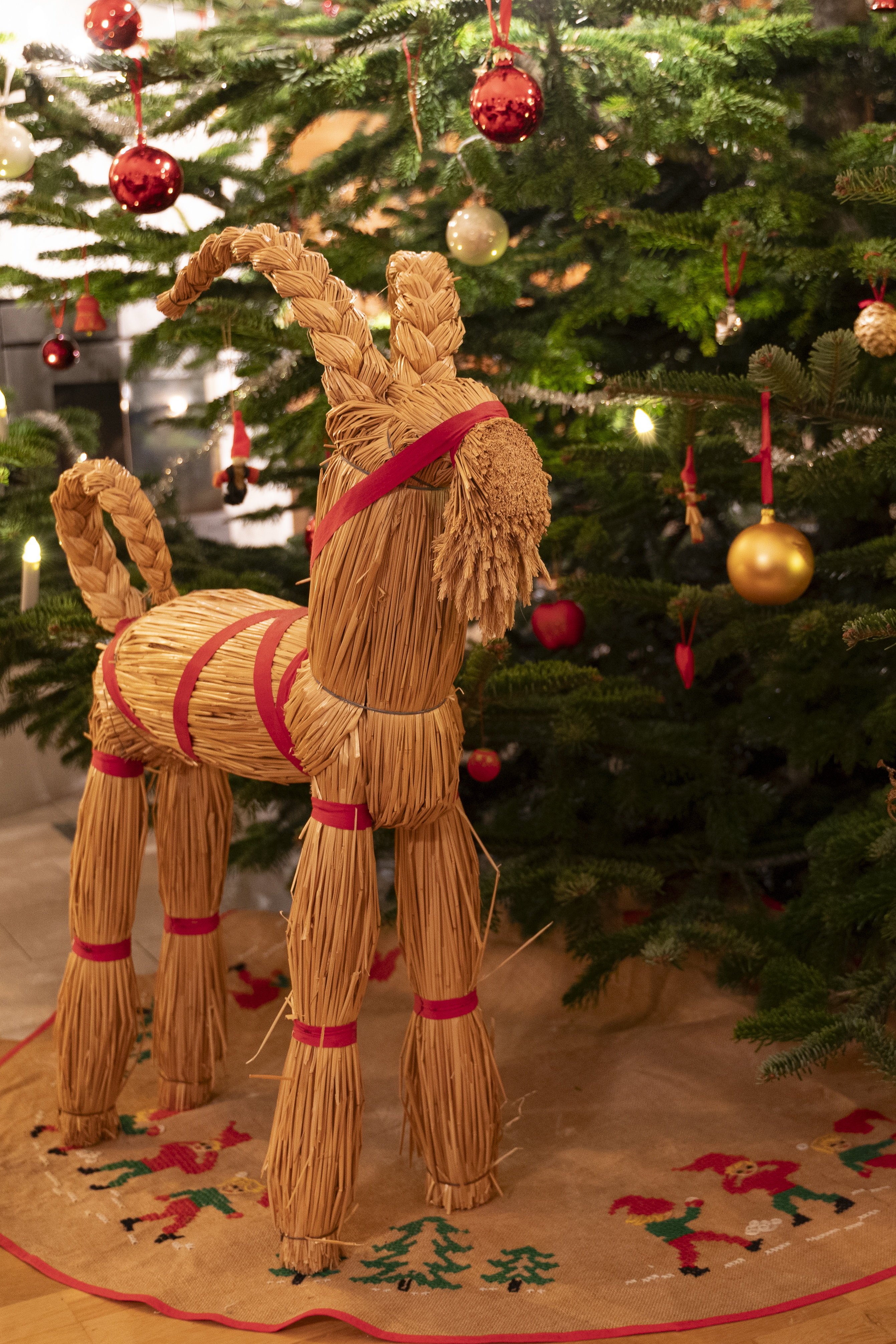 En julbock i halm står intill en gran dekorerad med julkulor.