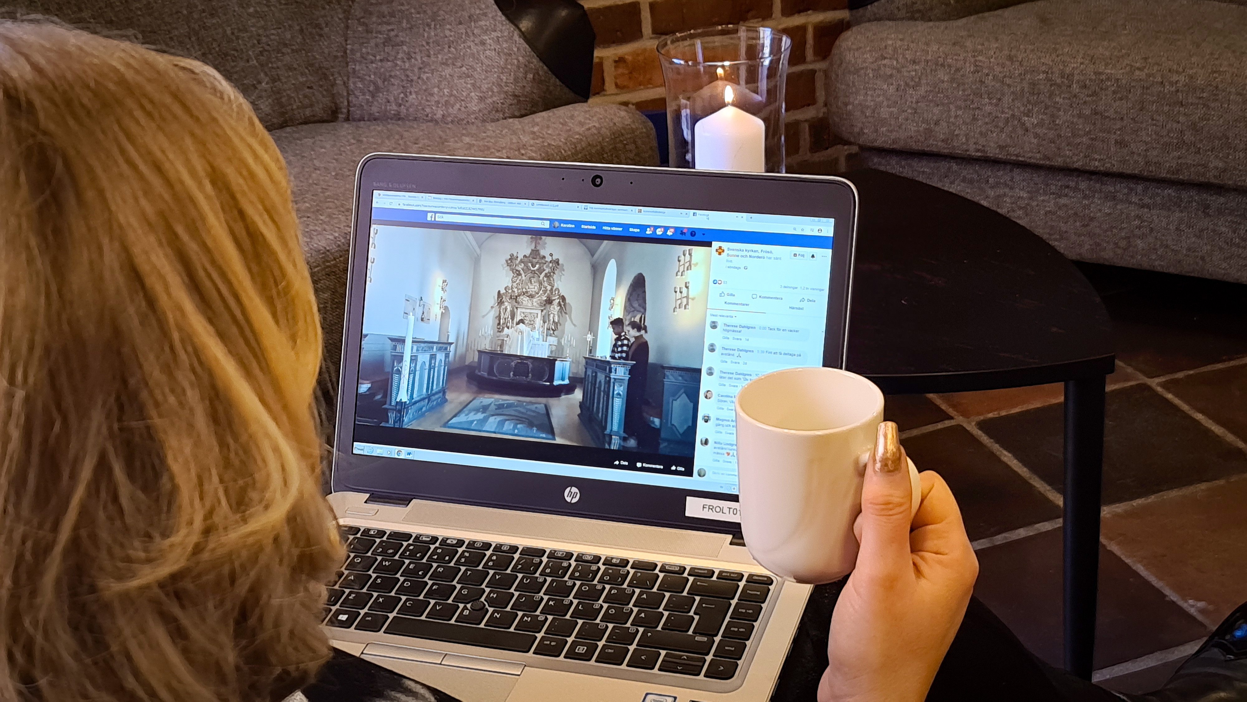 En person med en kaffekopp i handen tittar på en streamd gudstjänst på en laptop.