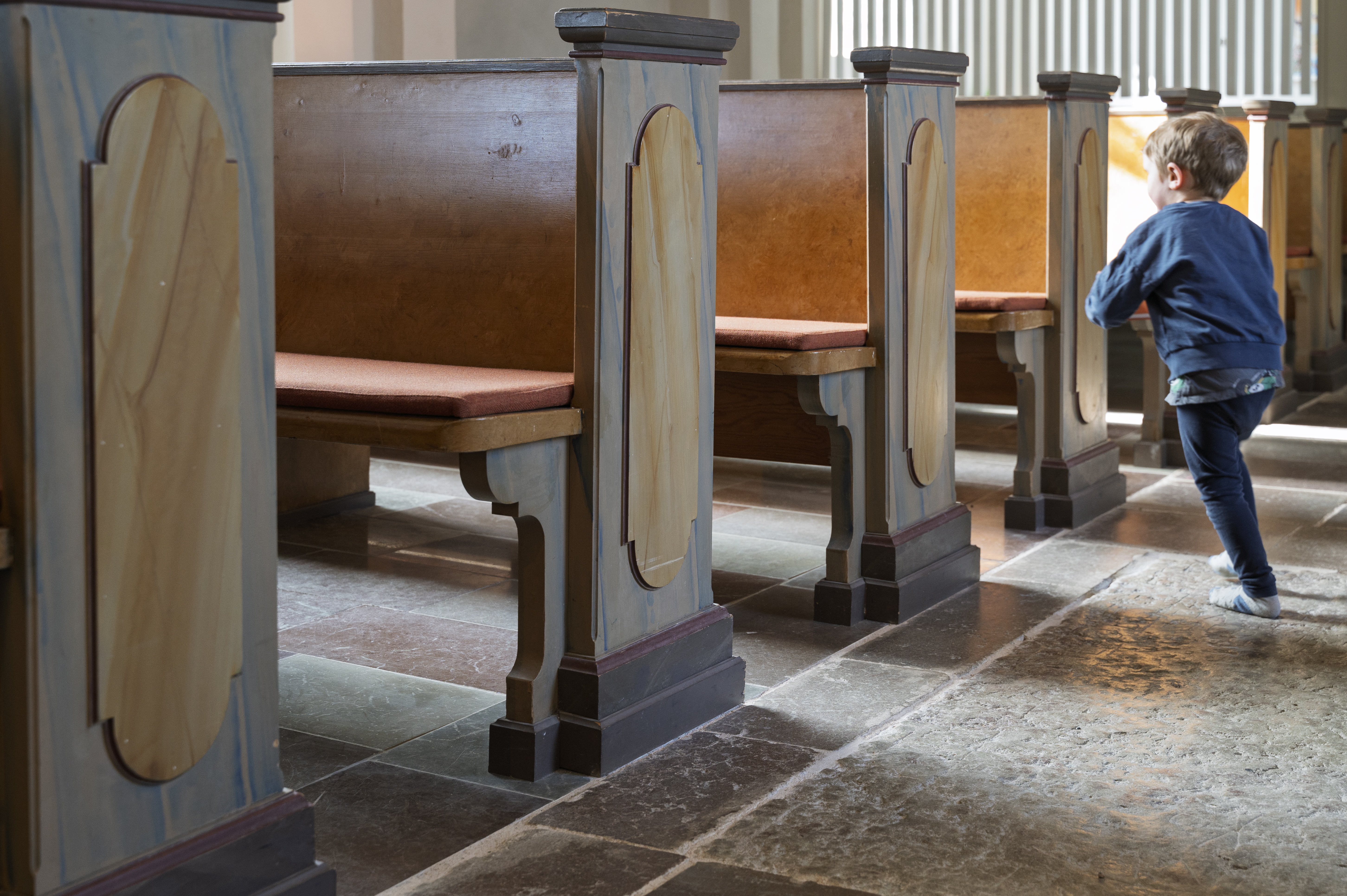 En liten pojke lekar bland kyrkbänkarna.