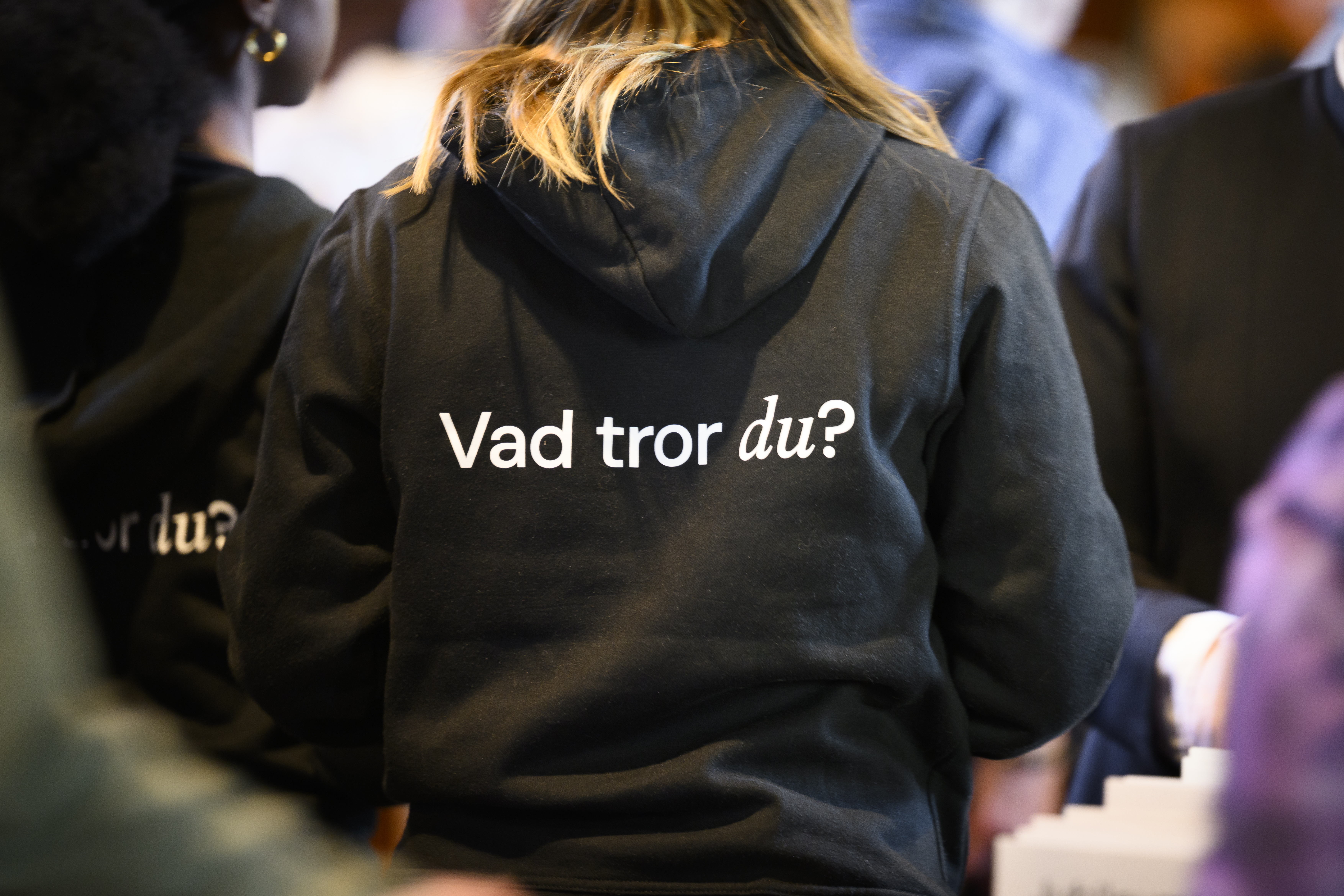 En person står med ryggen mot kameran, bär en svart hoodie med texten ”vad tror du?”.