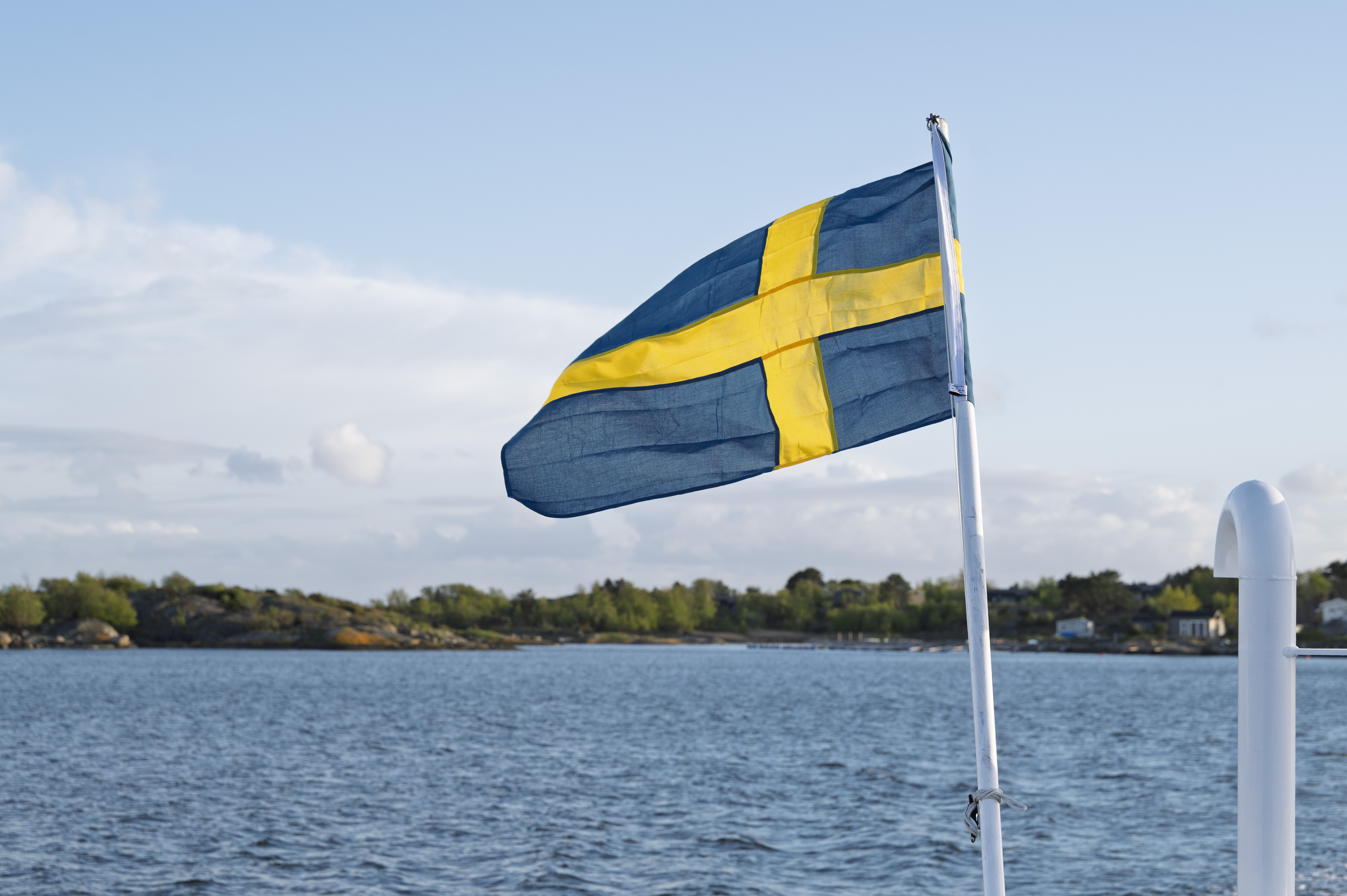 Svenska flaggan vajar på en båt. Skärgård i bakgrunden.