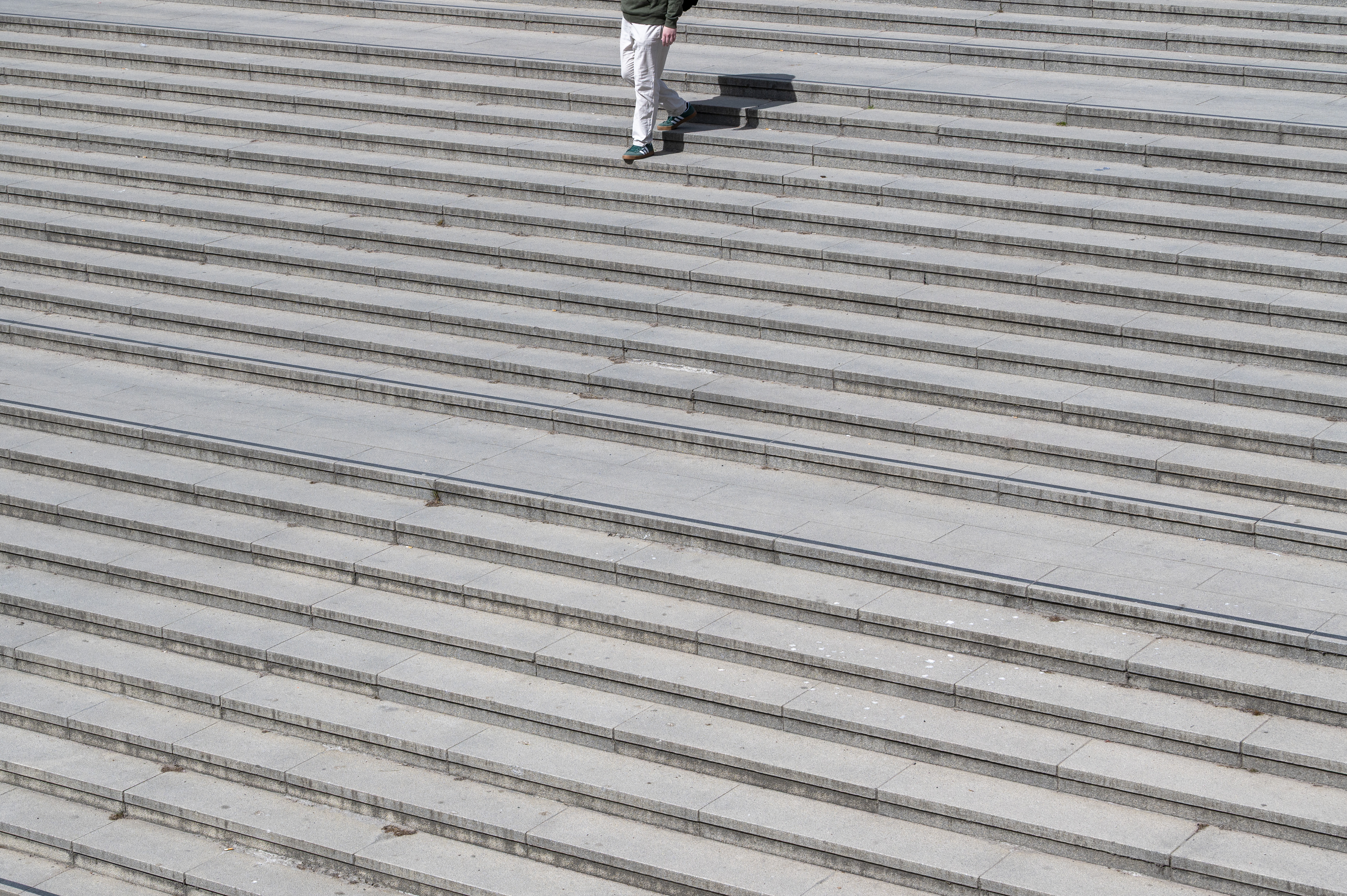 En person i vita byxor är utomhus på väg ner för en bred grå stentrappa.