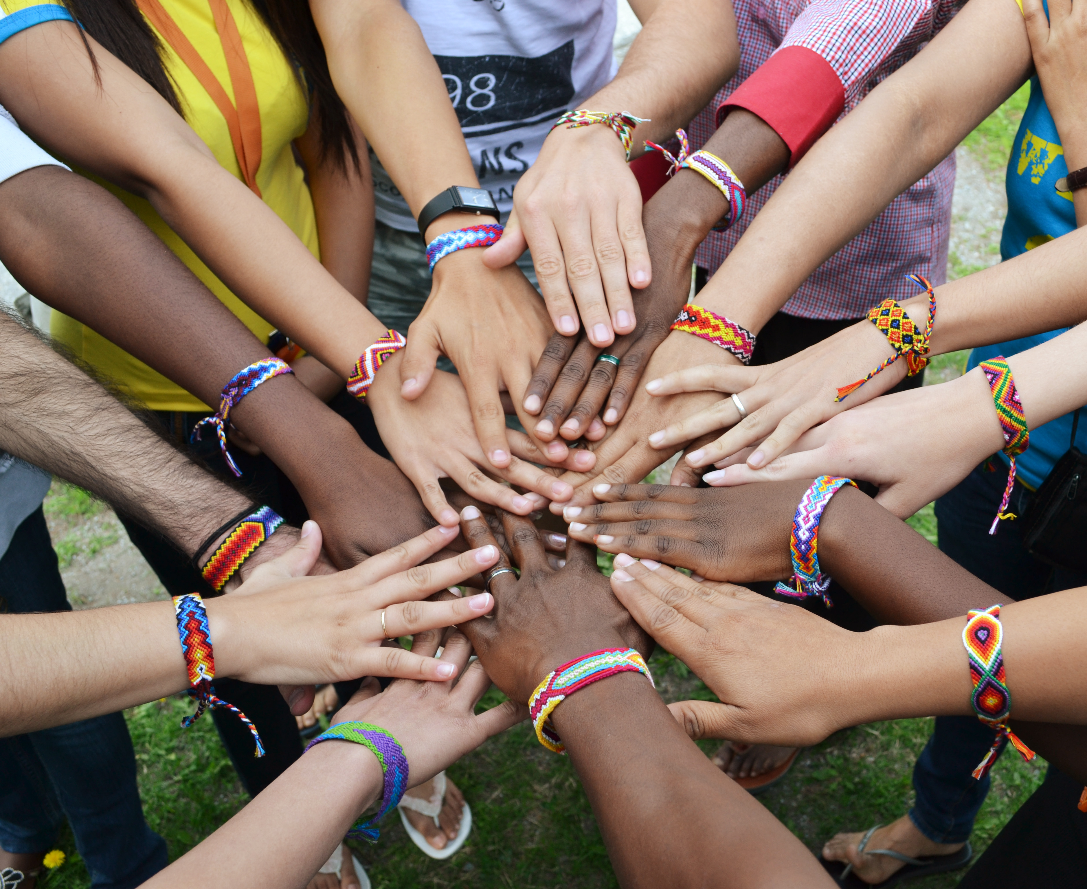 En grupp ungdomar med vänskapsarmband står i en klunga med händerna i mot mitten.