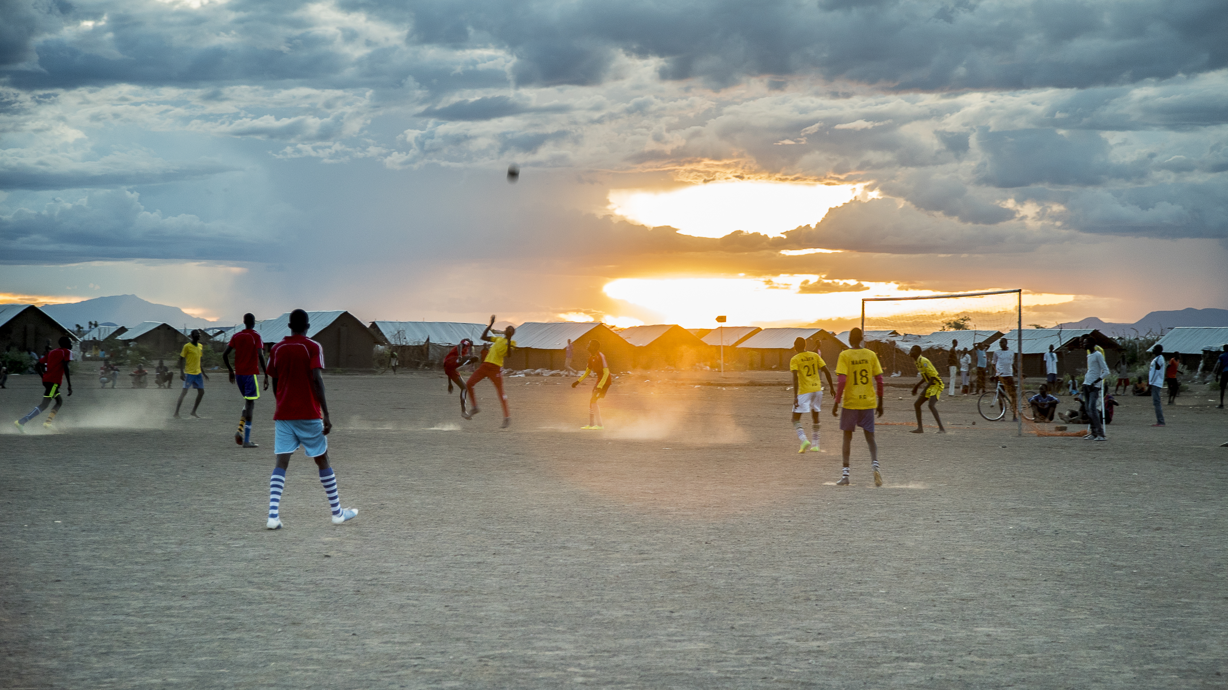 Solnedgång över en fotbollsplan fylld med spelare. 