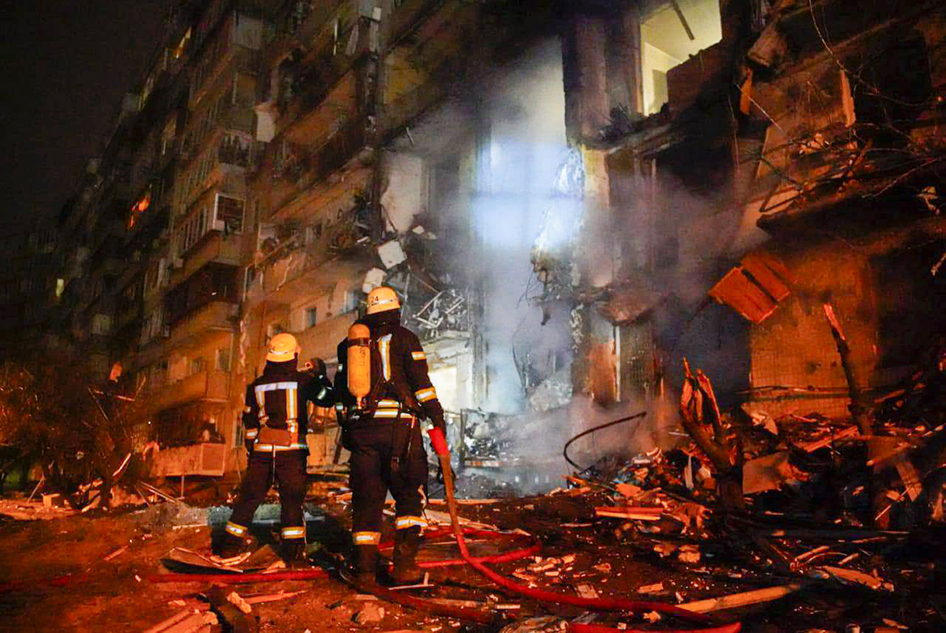 Två brandmän står och tittar på ett sönderbombat hus.