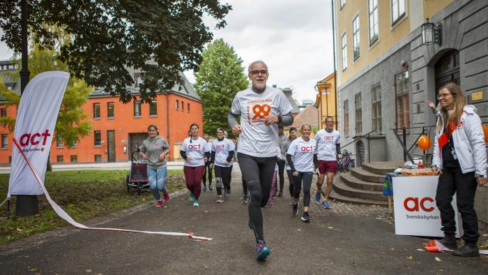 En grupp människor springer mot kameran. Det står Världens Barn eller Act Svenska kyrkan på deras kläder. 