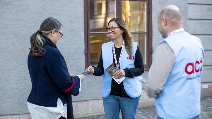 Två personer i Act Svenska kyrkans blåa väst delar ut informationsmaterial.