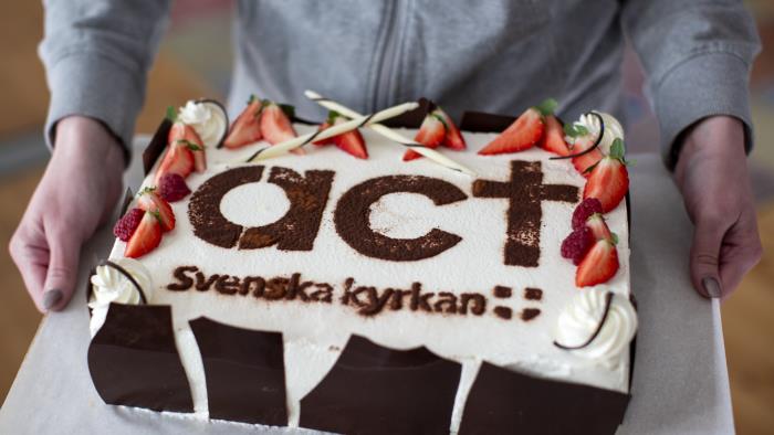Tåtra med jordgubbar och grädde. På tårtan står det Act Svenska kyrkan.