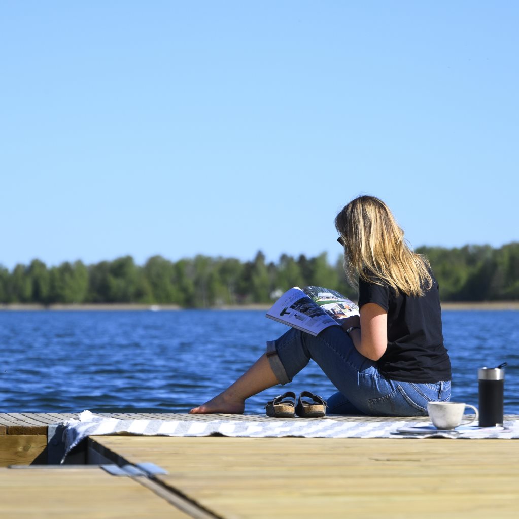 Kvinna sitter på en brygga och läser en tidning.