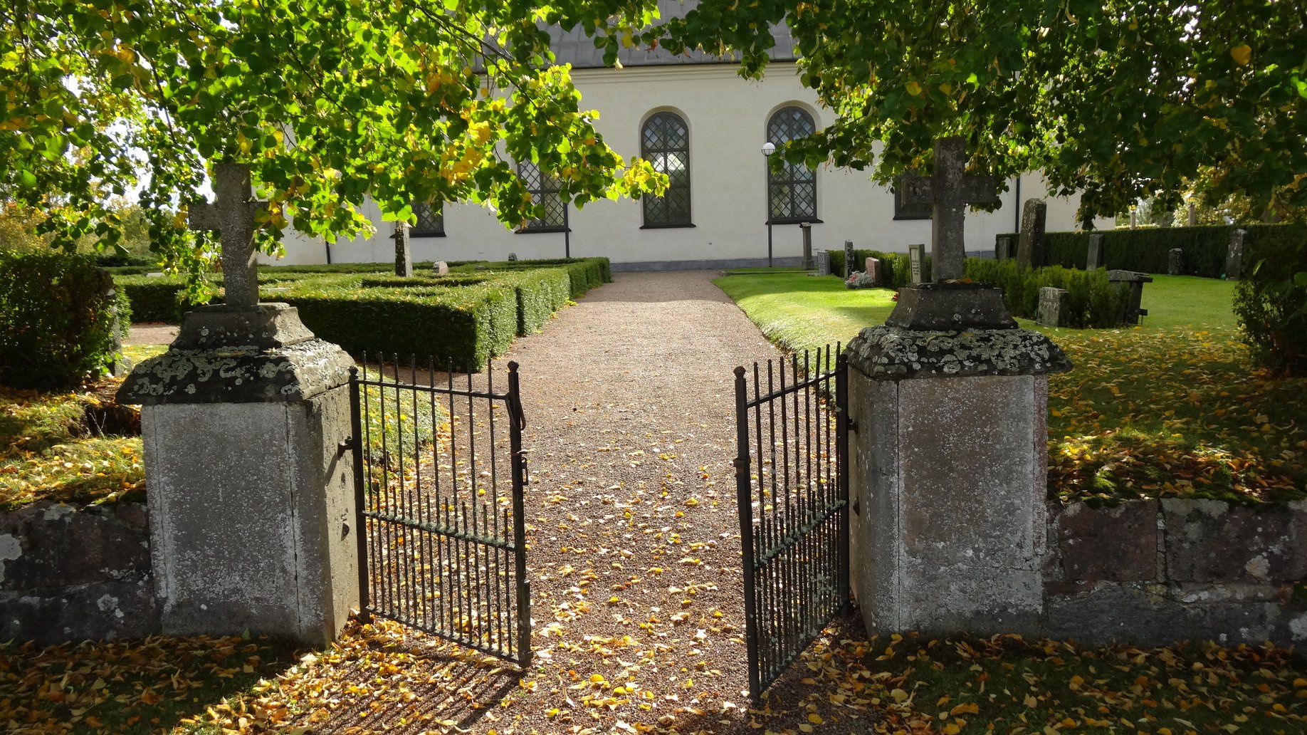 En öppen kyrkogårdsgrind mot grusgången till Rinna kyrka