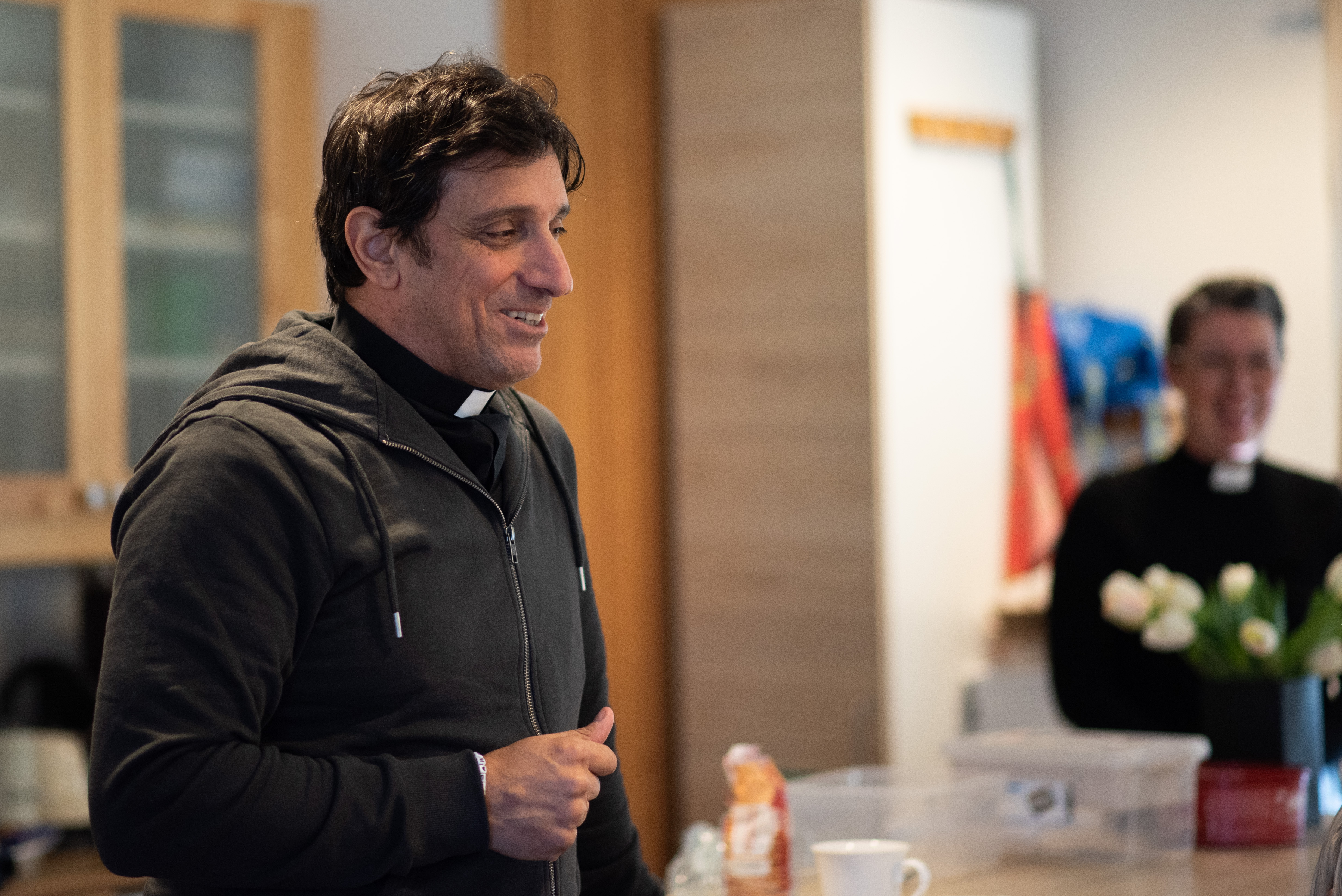 En man med prästkrage talar inför besökare på ett kafé.