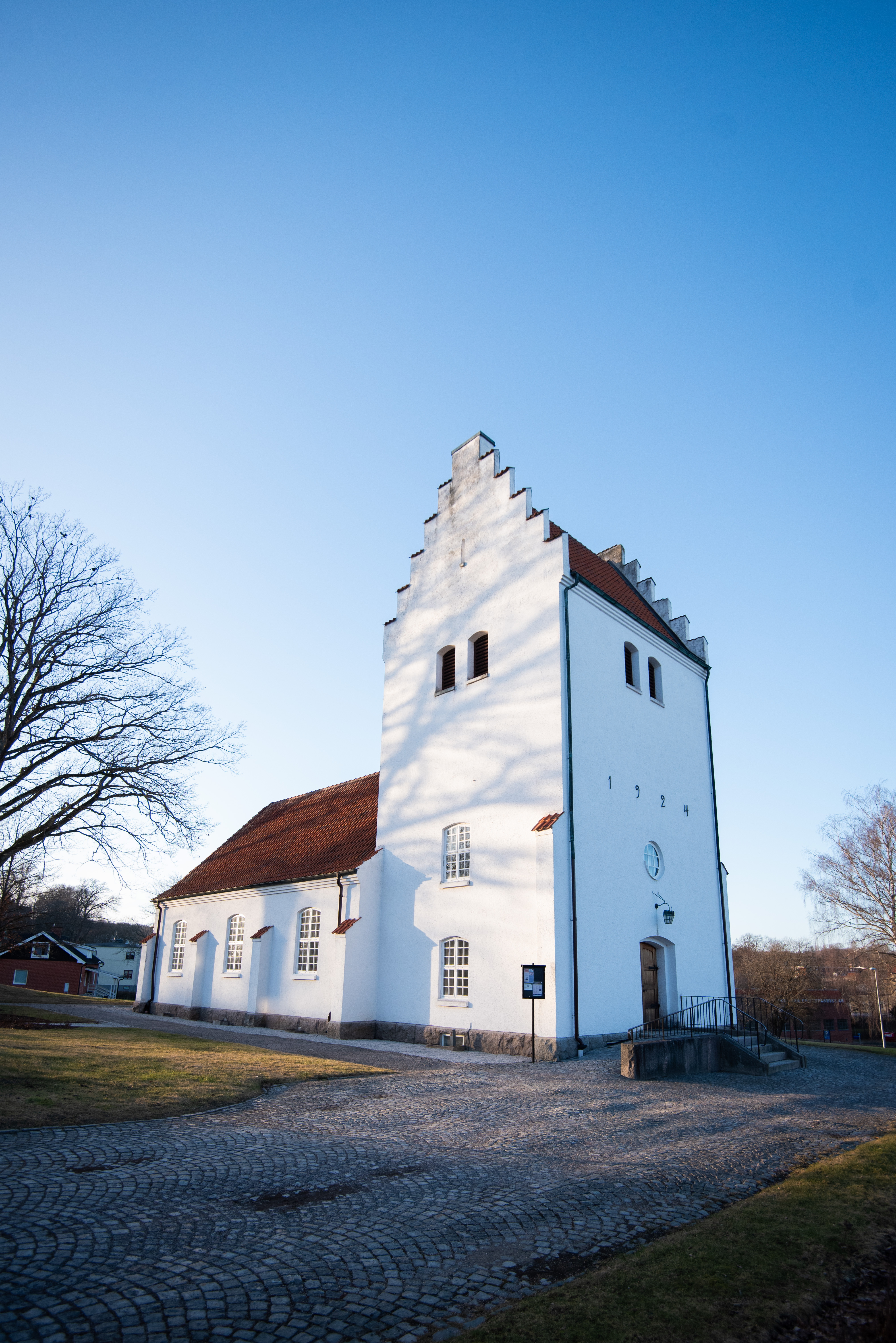 En vit kyrka i en by. Kvällssolen lyser och det är vår.