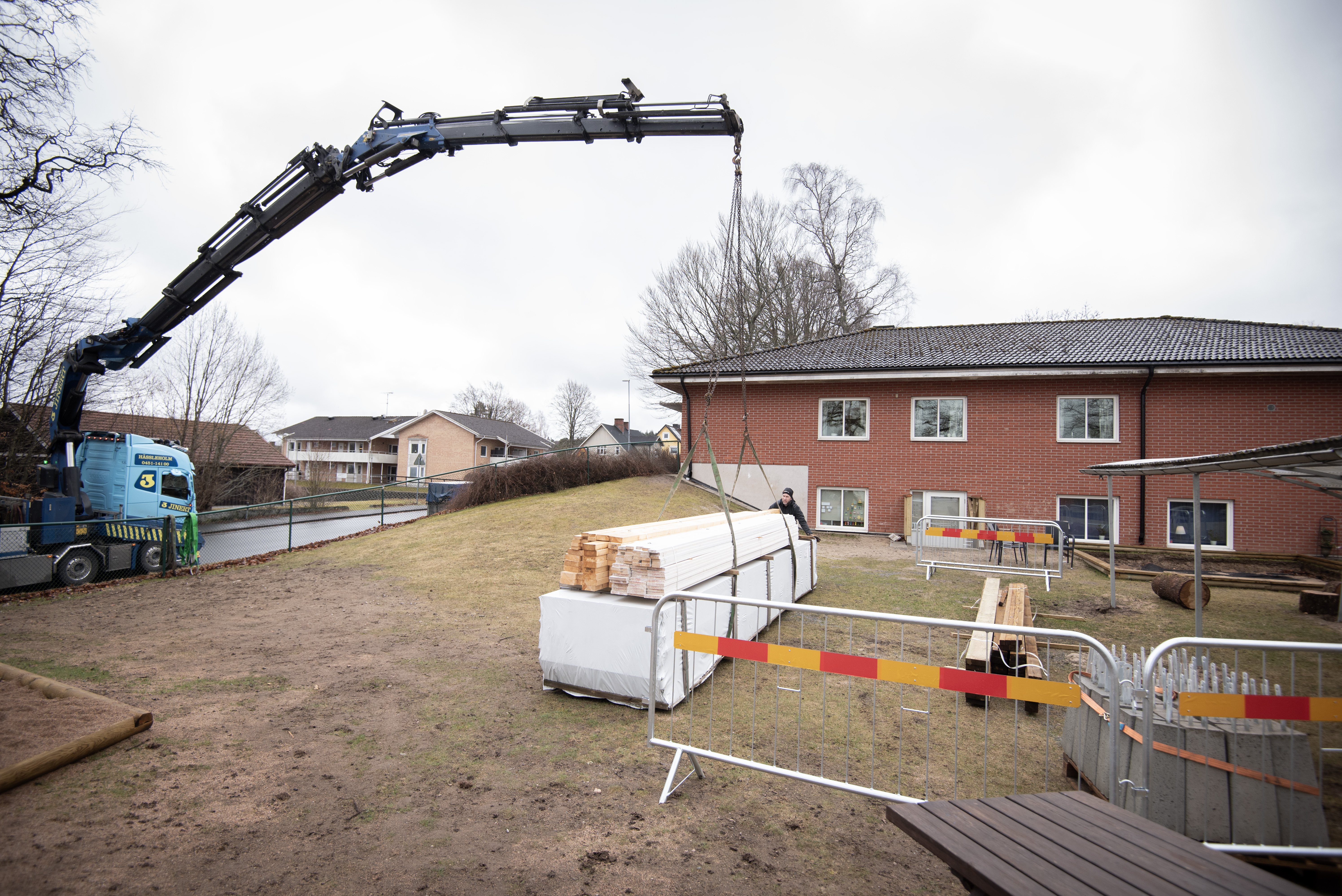 En lyftkran ställer ner ett stort paket med trämaterial på en lekplats.