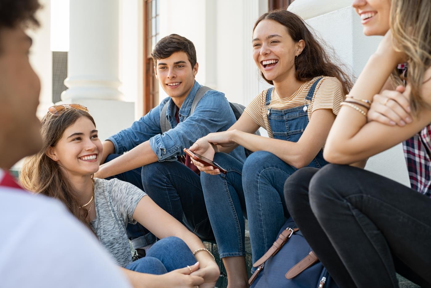 Fyra ungdomar i gymnasieålder sitter tillsammans på en trappa, pratar och skrattar.