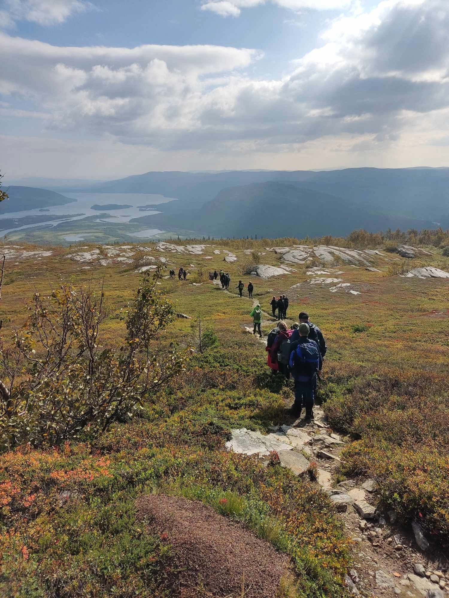 Lägerdeltagare går på en stig. Framför dem ser man berg och en dal med vatten. 