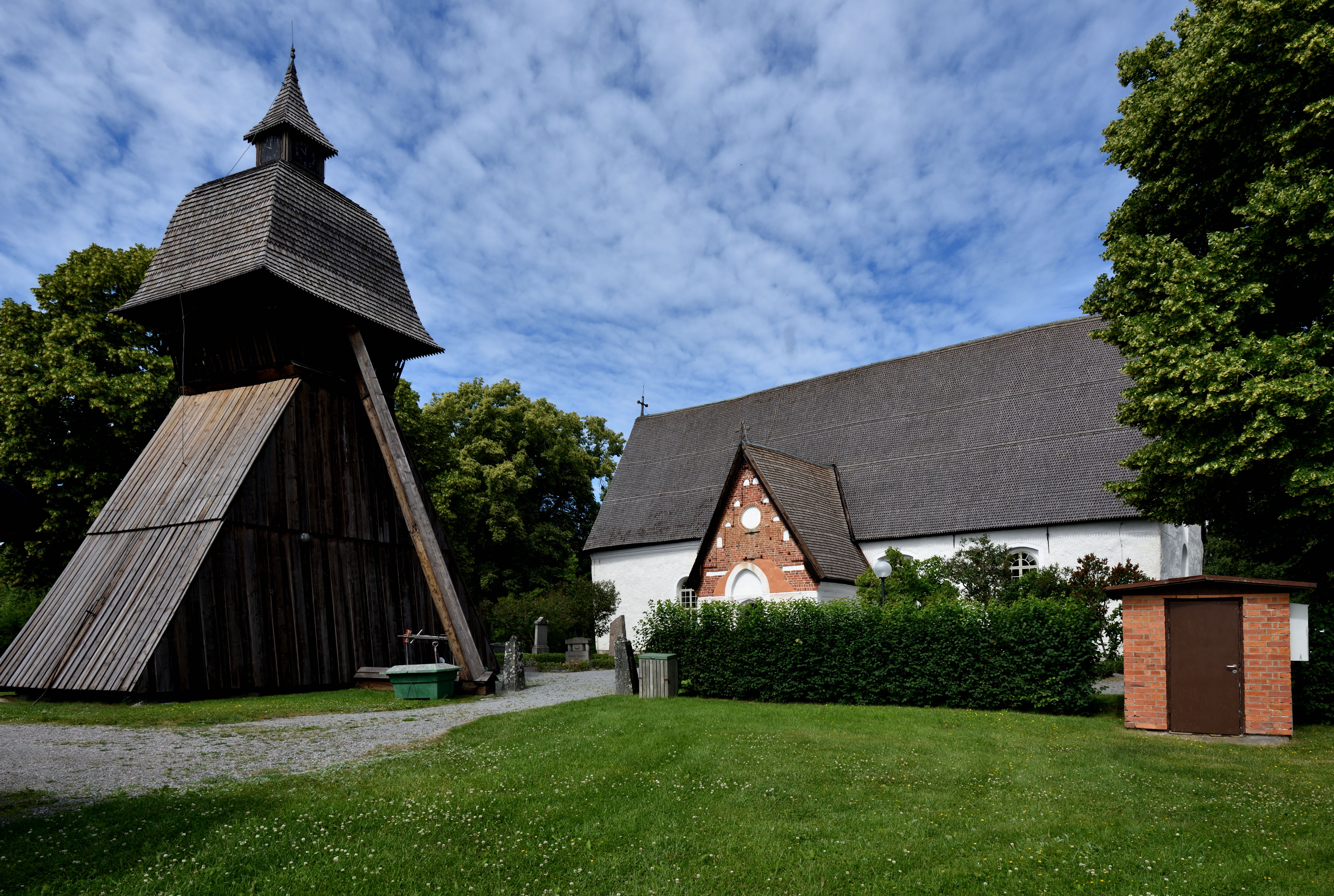 En gammal vit stenkyrka och en klockstapel i trä.