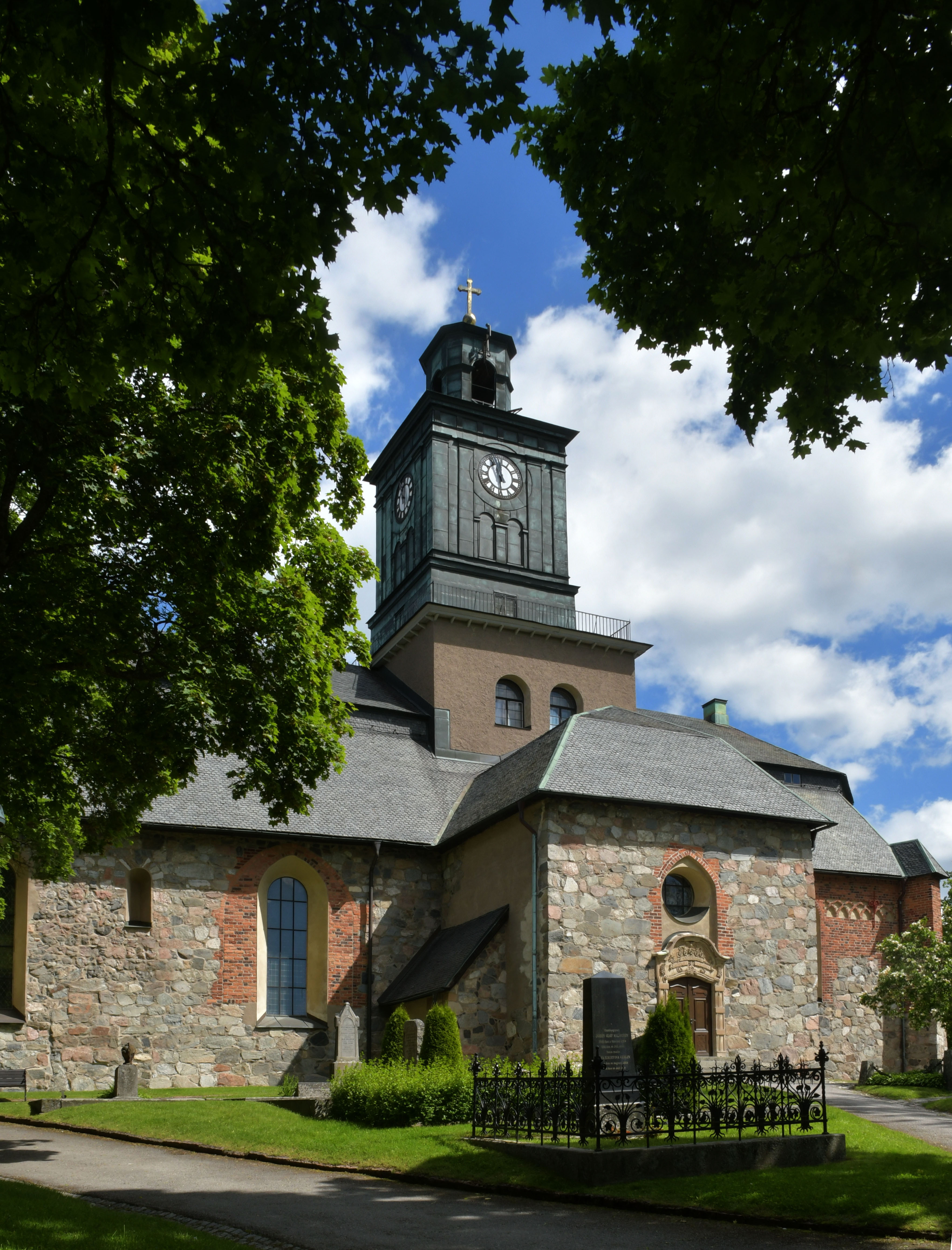 Ett kyrktorn med gröna lövträd i förgrunden.