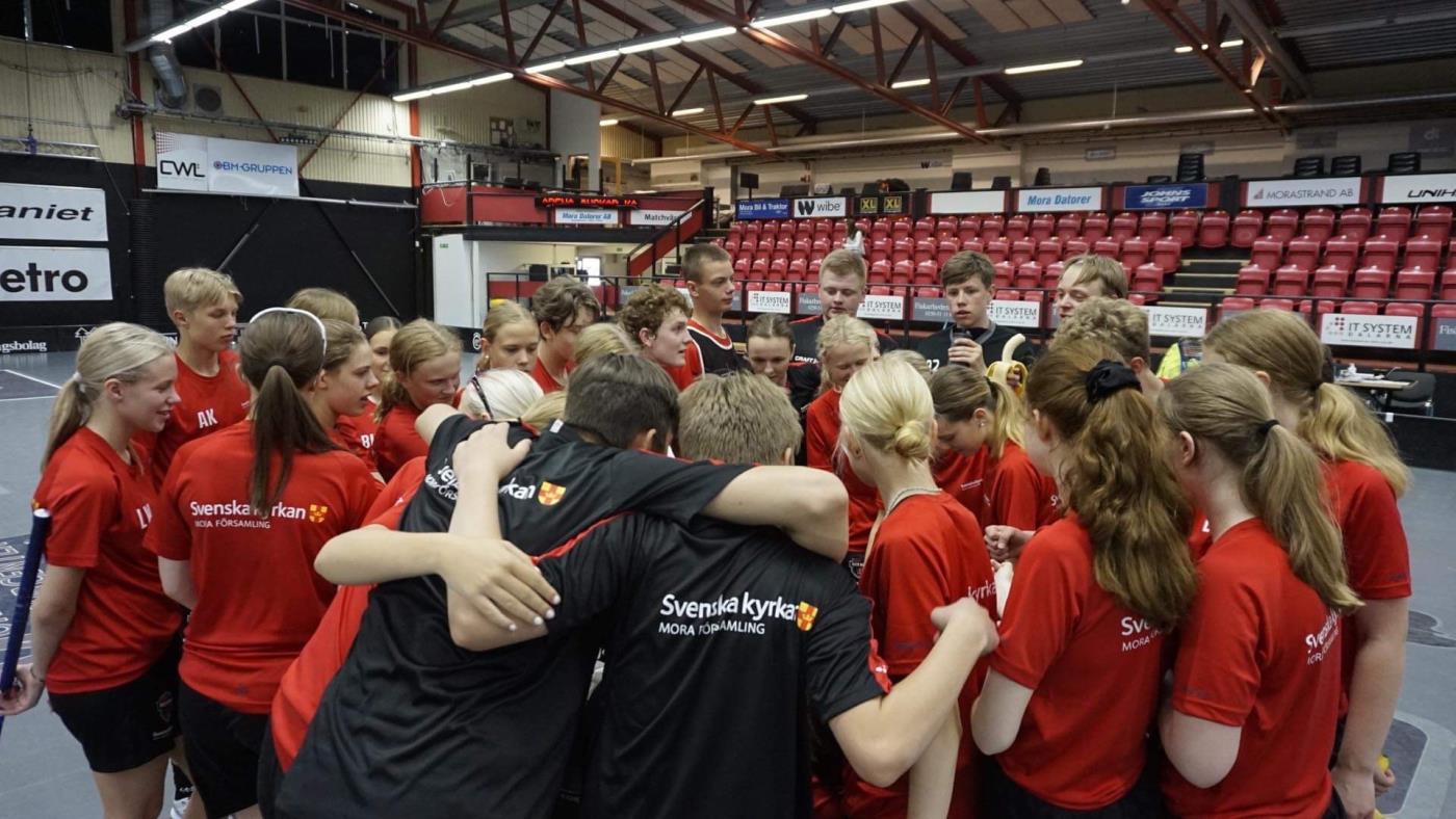 Innebandy konfirmationsgrupp samlas i ring för pepp. Träningströjor har Svenska kyrkan Mora församlings logo på ryggen