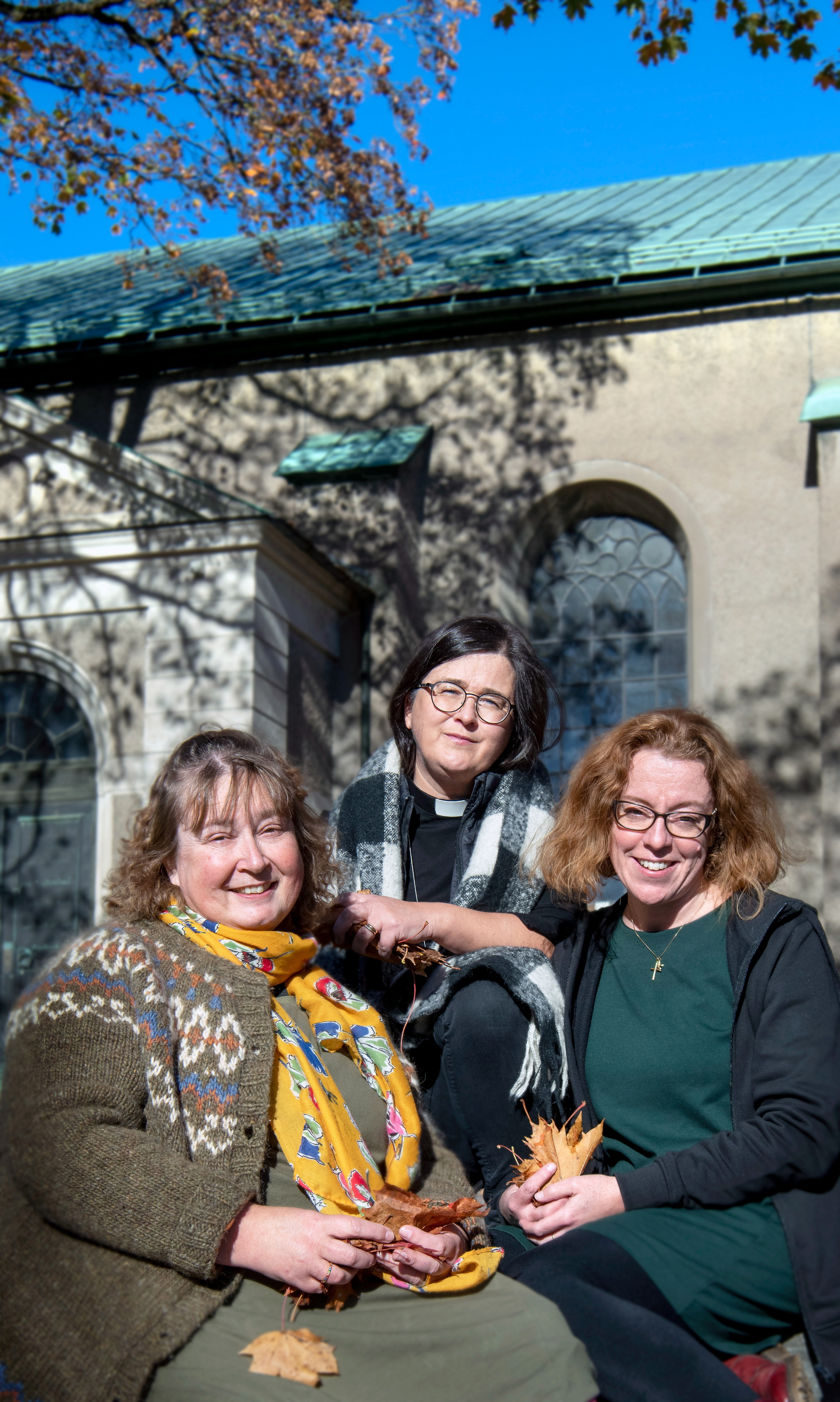 Tre kvinnor på trappa utanför kyrka. Höstlöv och blå himmel.
