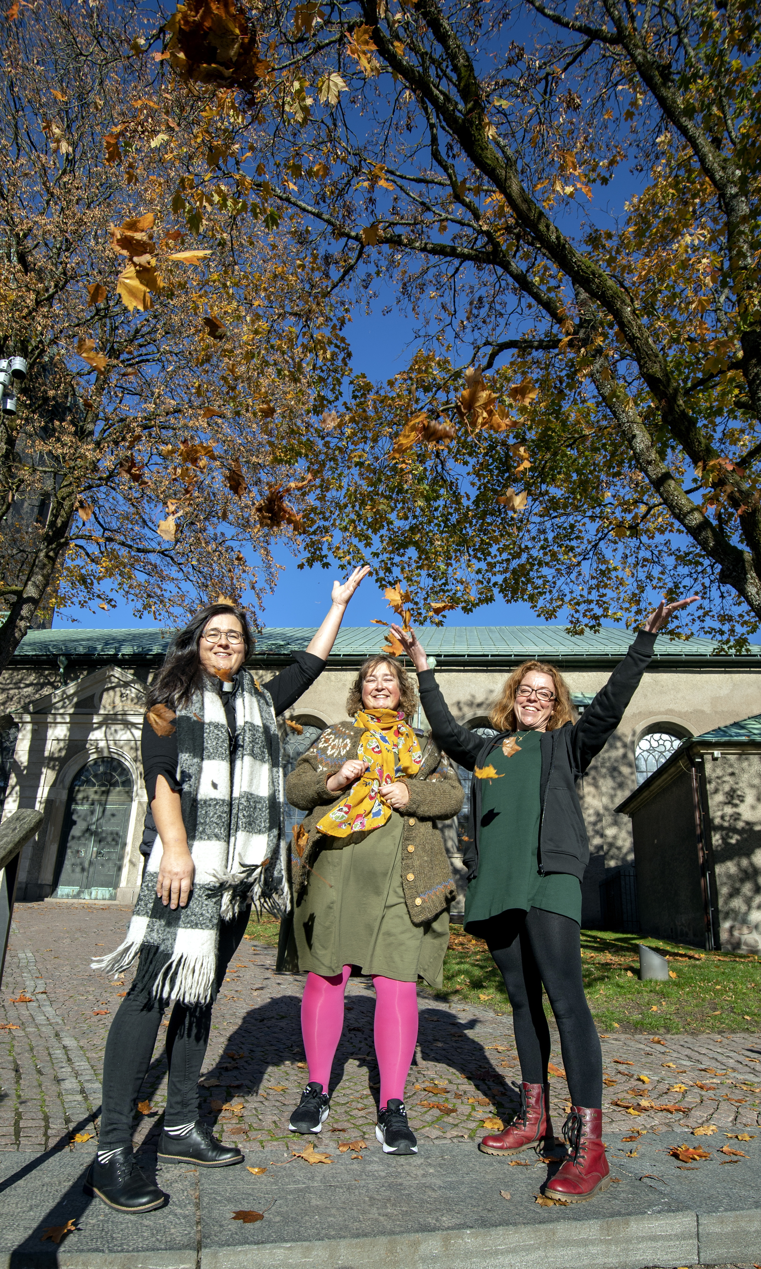 Tre kvinnor på trappa utanför kyrka. Höstlöv och blå himmel.