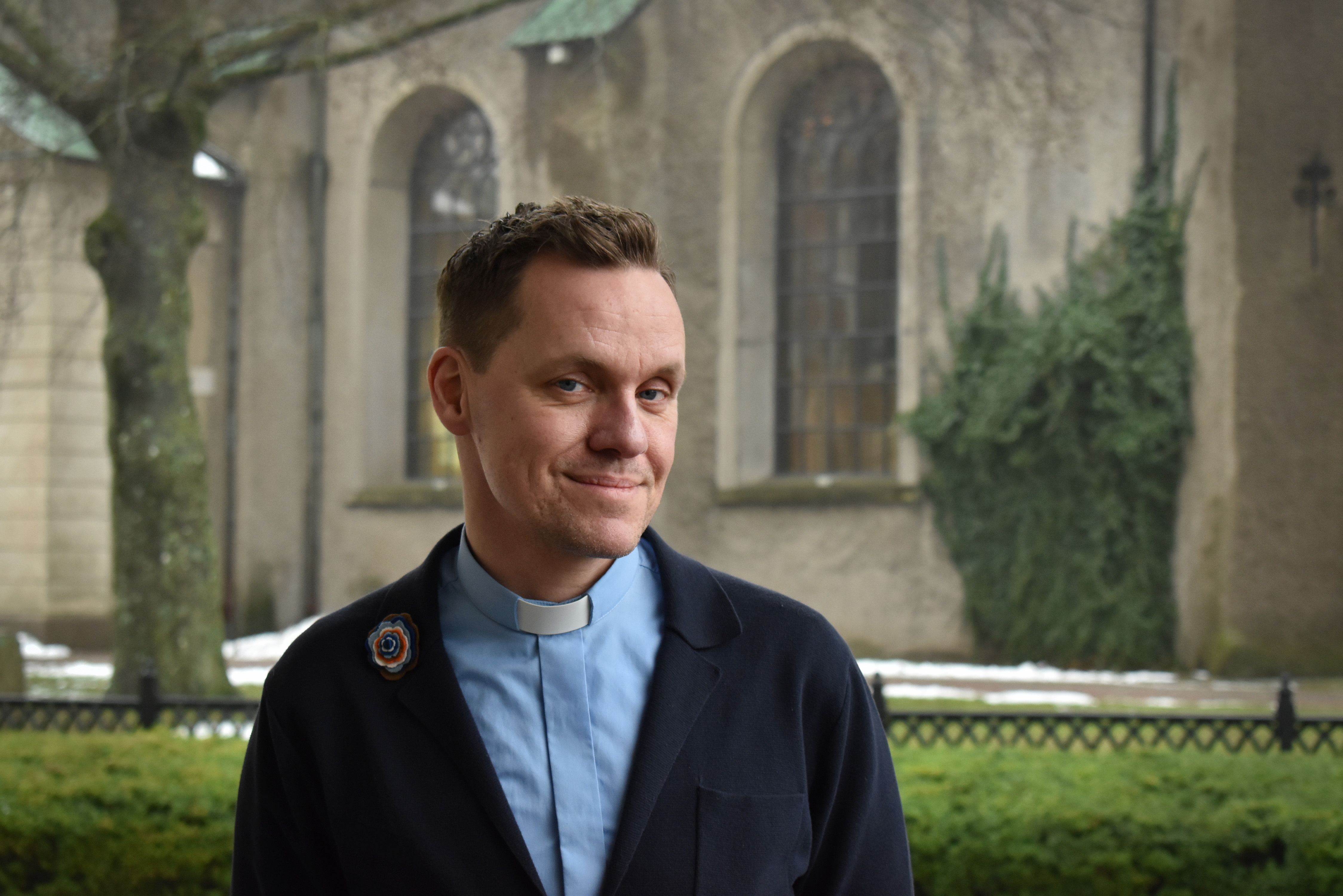 Porträttbild. Präst framför kyrka.