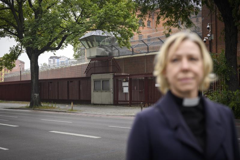 En kvinnlig präst står på gatan utanför portarna till ett fängelse.