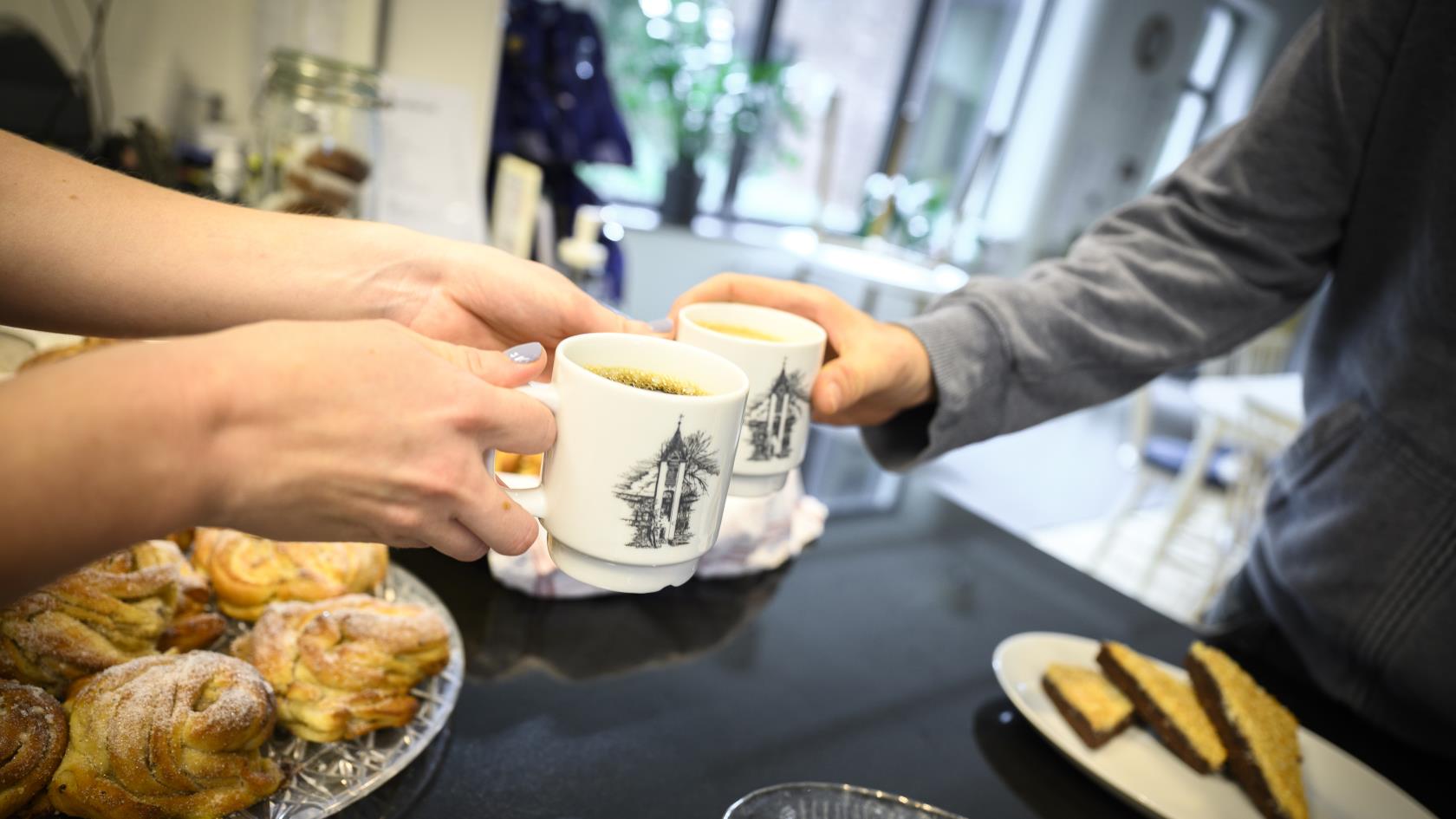 Någon räcker över en kopp kaffe över ett fikabord.