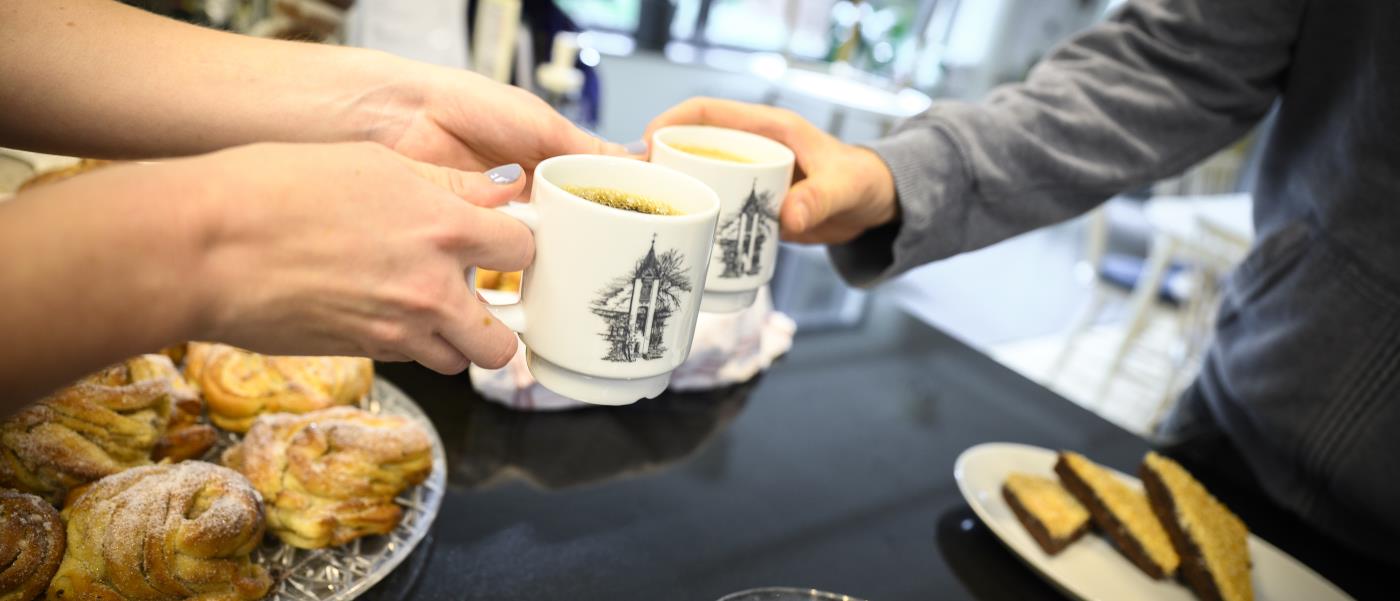 Någon räcker över en kopp kaffe över ett fikabord.