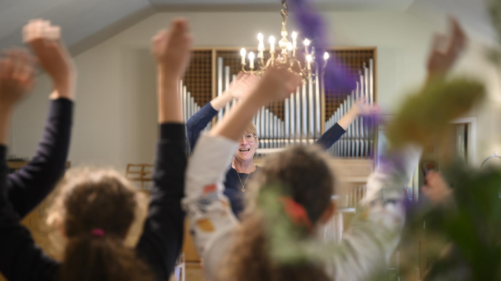 Några ungdomar står i en kyrka och viftar med armarna i luften. En kvinna står framför dem och gör likadant.
