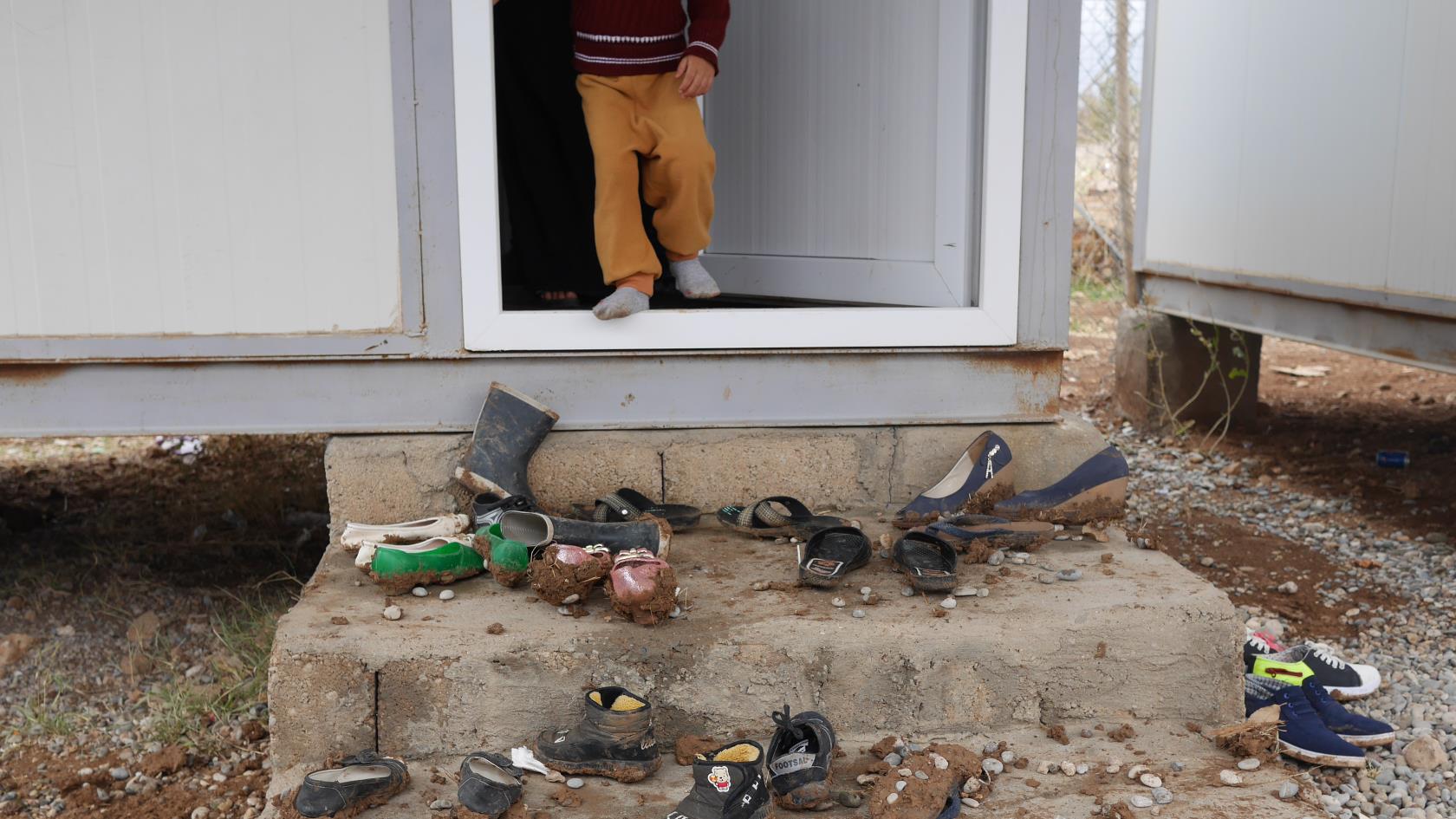Ett barn öppnar dörren till en enkel bostad. På trappan utanför ligger mängder av leriga skor.