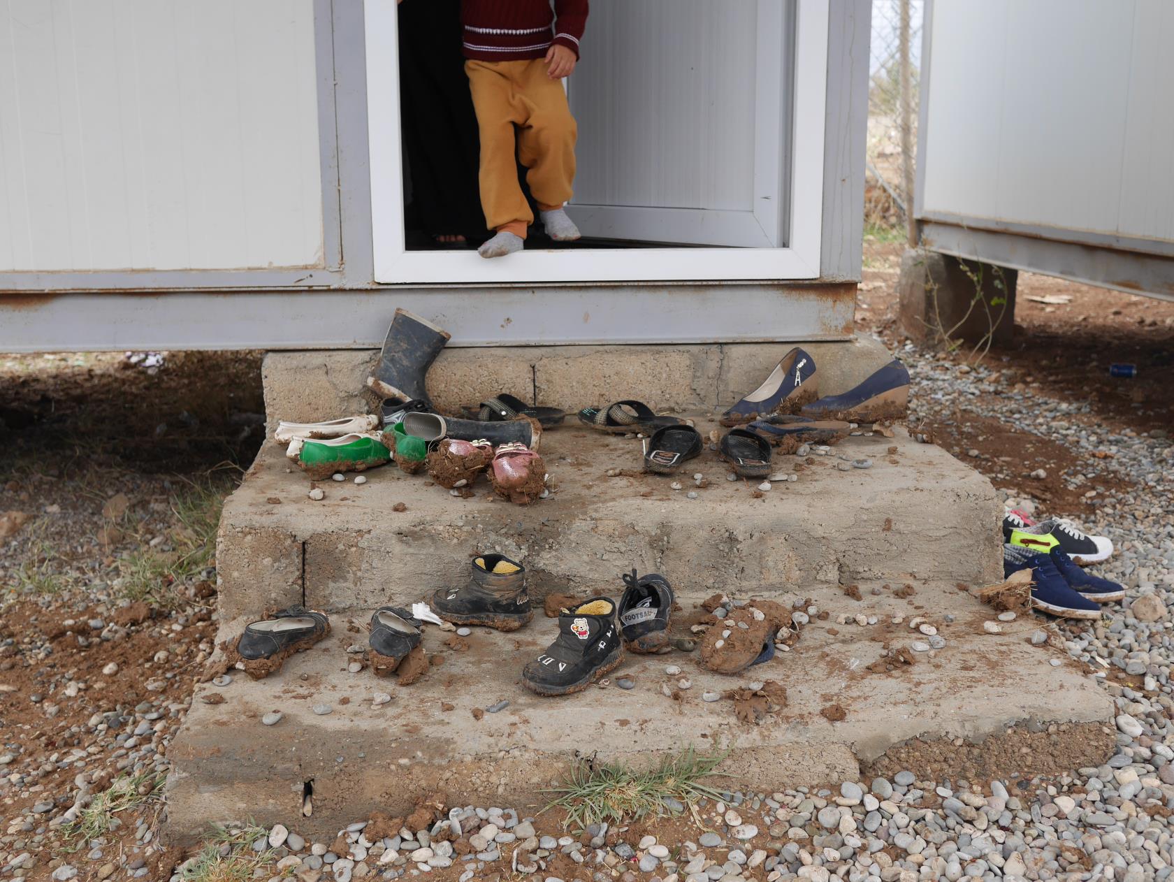 Ett barn öppnar en dörr till en mycket enkel bostad. Utanför på trappan ligger en mängd leriga skor.