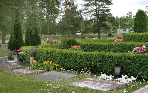 Några gravar på Norra kyrkogården med liggande gravsten, gravarna är så kallade kistgravar, bakom gravstenarna går en låg häck med blommor på och runt omkring syns träd och buskar.