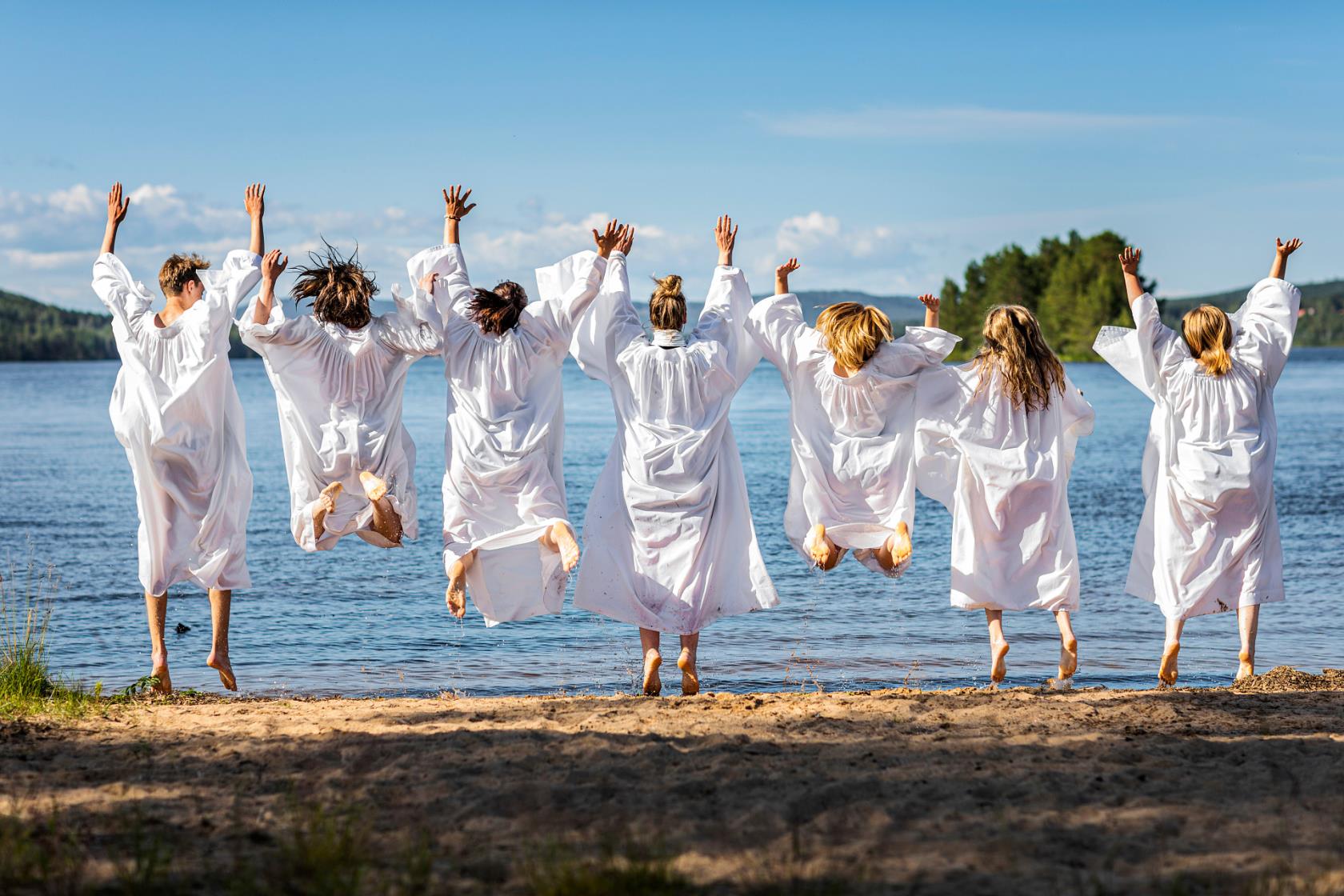 Konfirmander står och hoppar glatt vid strandkant