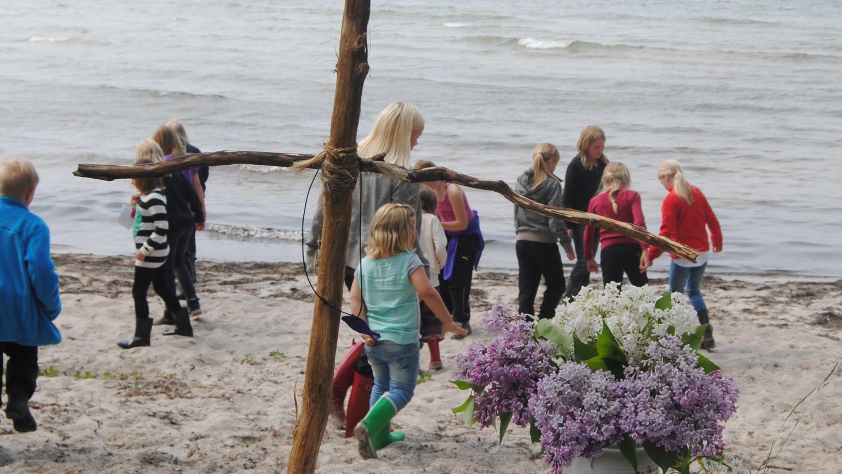 Ett träkors på stranden, barn leker i bakgrunden